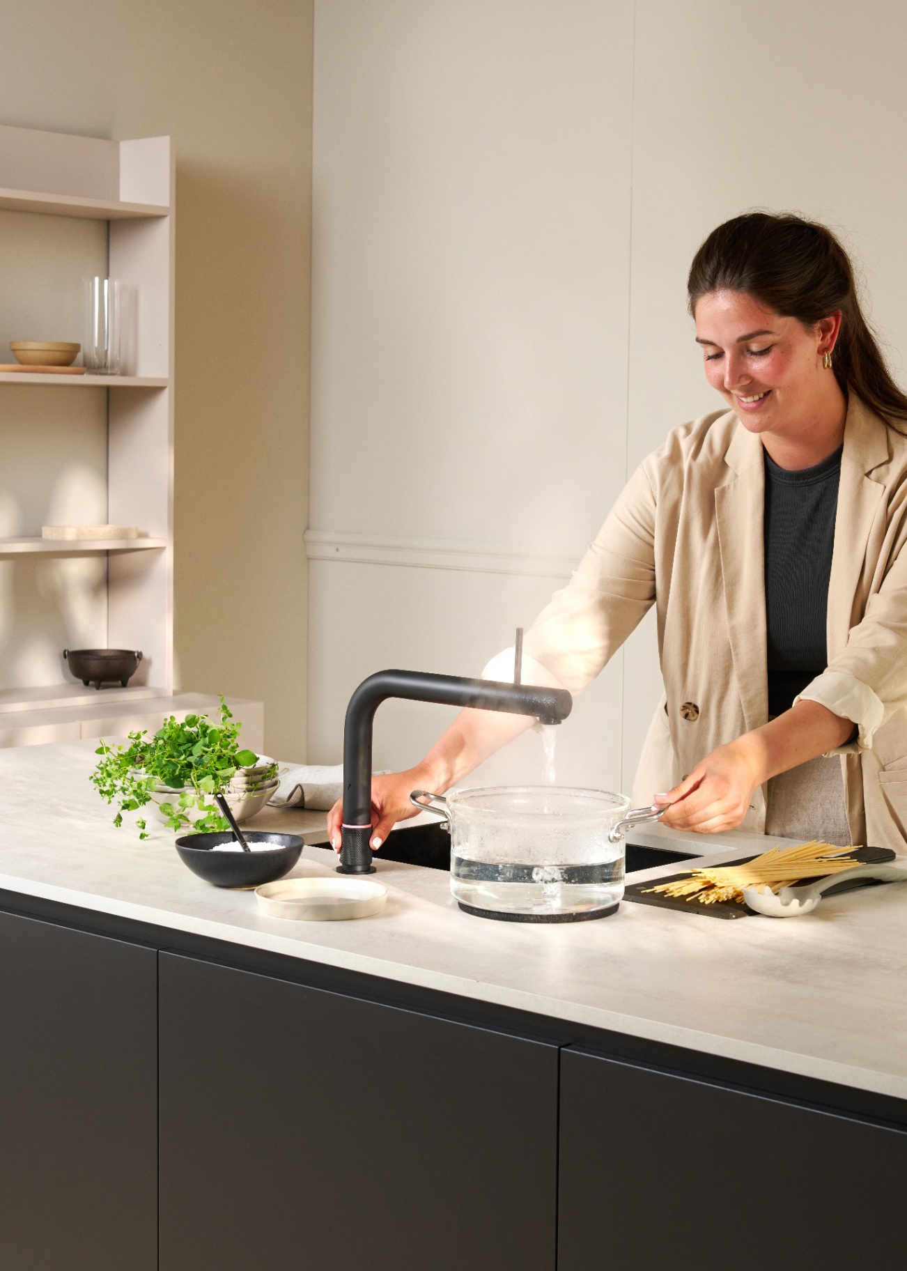 Quooker Front in matte black boiling water tap — pouring 100 °C boiling water, cooking pasta in a real customer kitchen. Genuine Quooker product supplied by Watertap.eu.