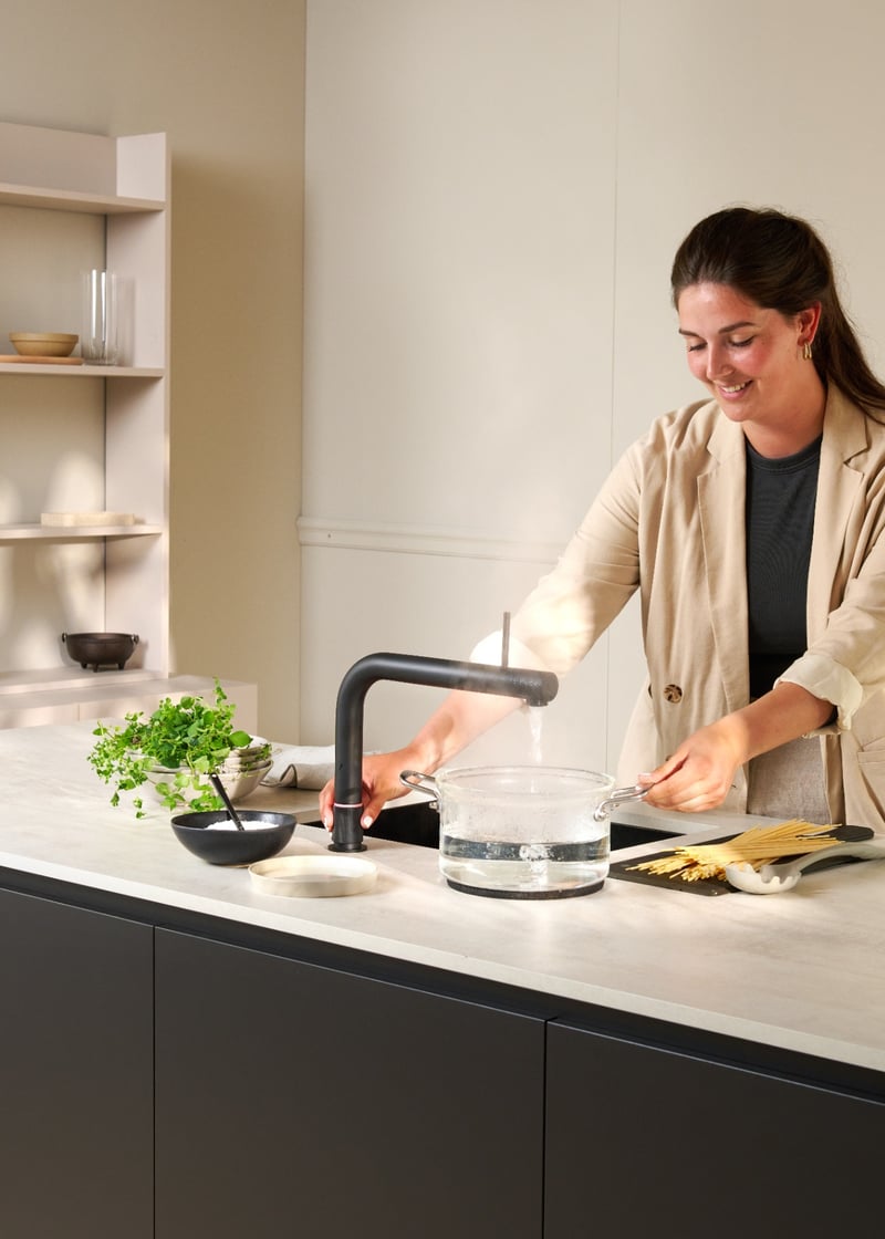 Quooker Front in matte black boiling water tap — pouring 100 °C boiling water, cooking pasta in a real customer kitchen. Genuine Quooker product supplied by Watertap.eu.