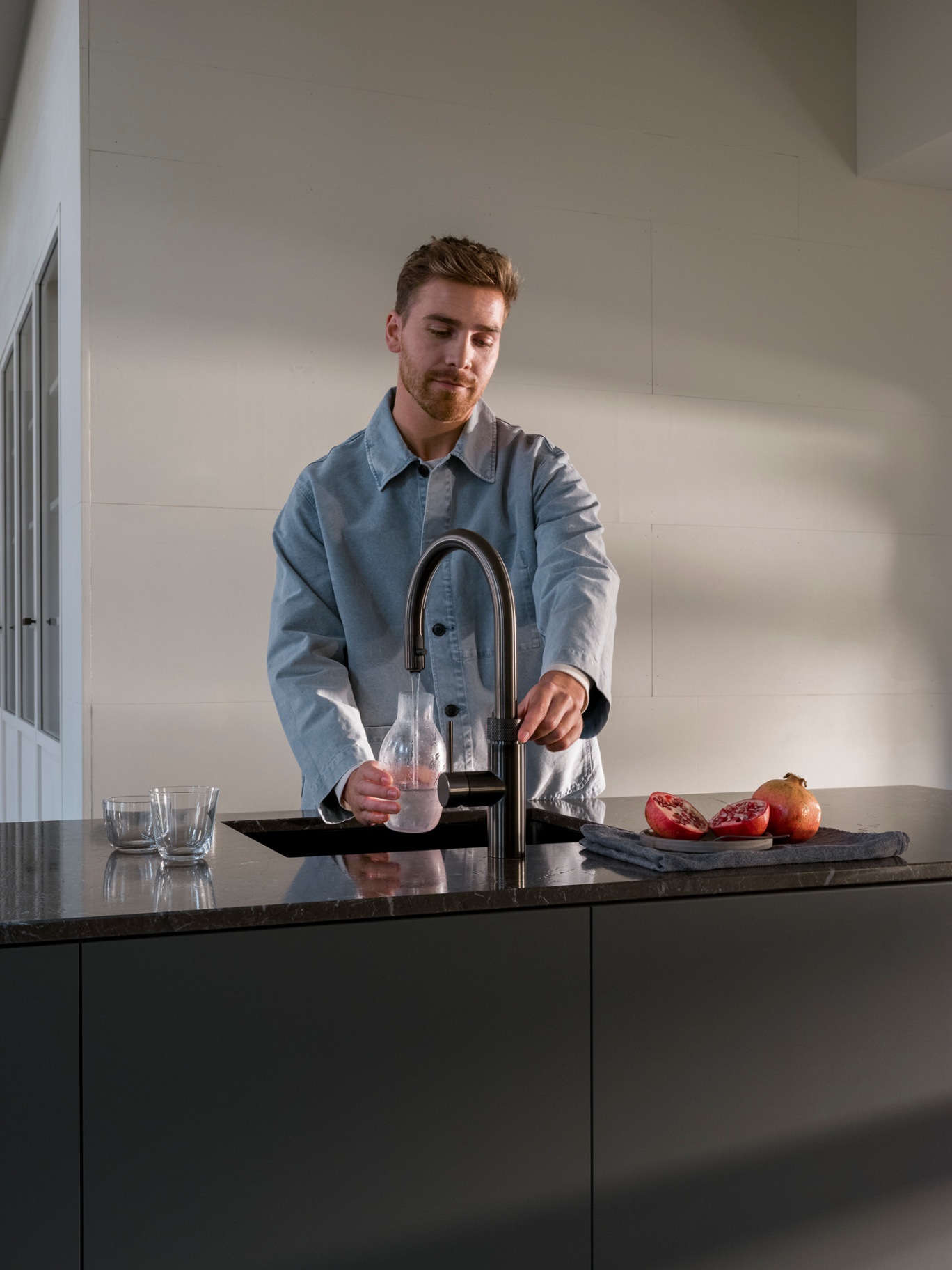 Man filling a carafe with chilled water at a Flex Round gunmetal Quooker beside pomegranate