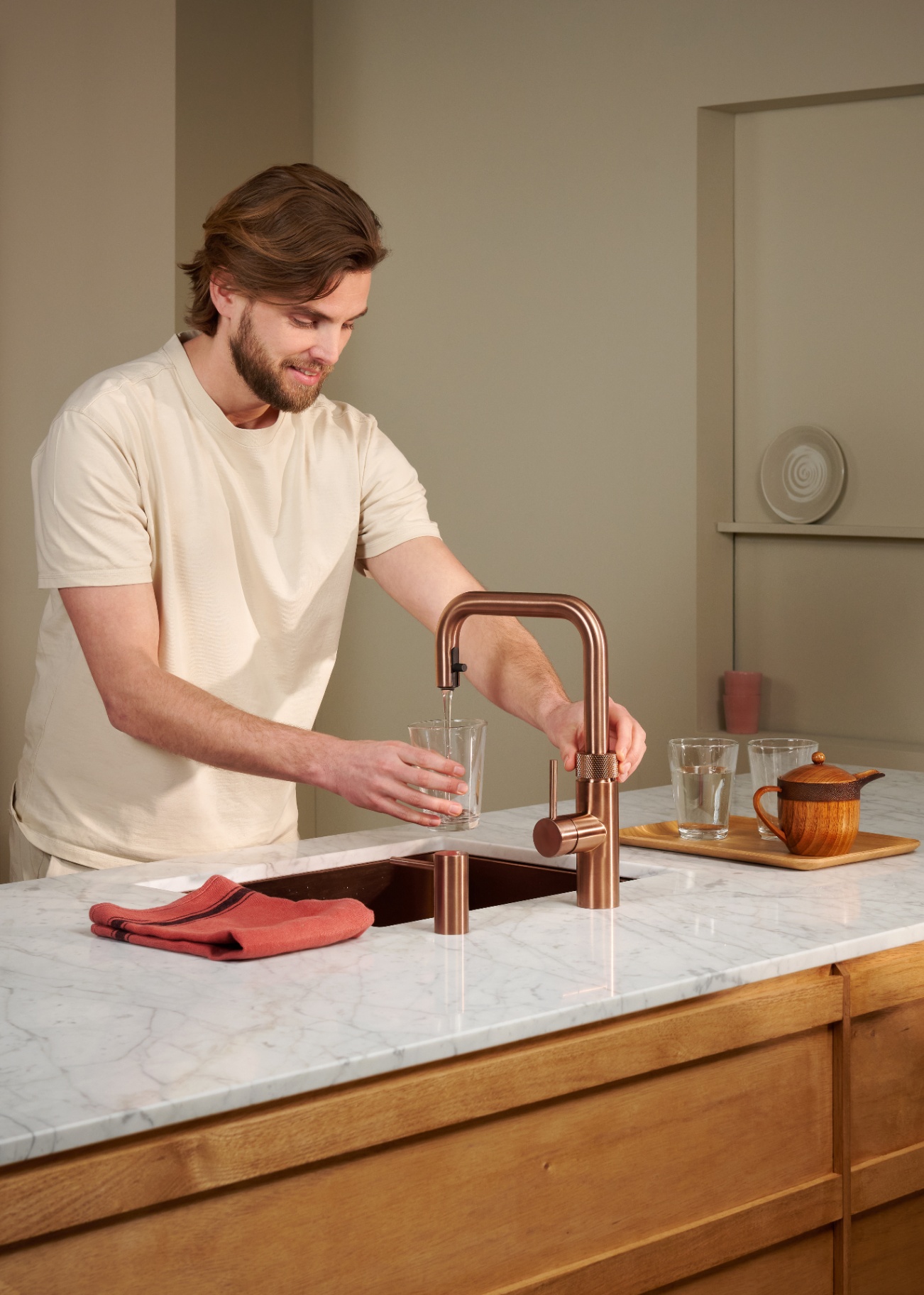 Man filling a glass of chilled water at a Flex Square rose copper Quooker on Carrara marble