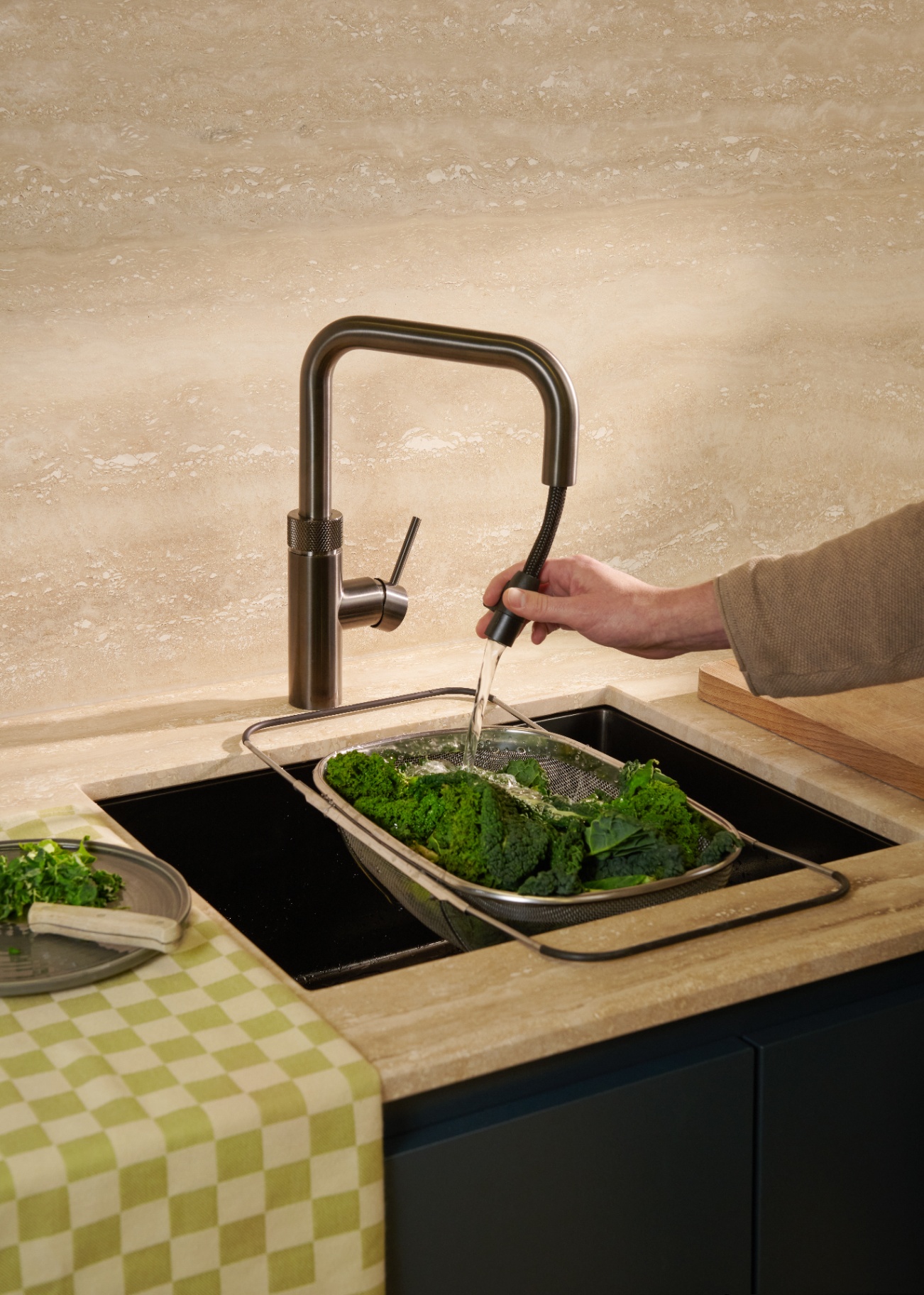Man rinsing kale in a colander with the pull-out hose of a Flex Square gun metal Quooker on travertine