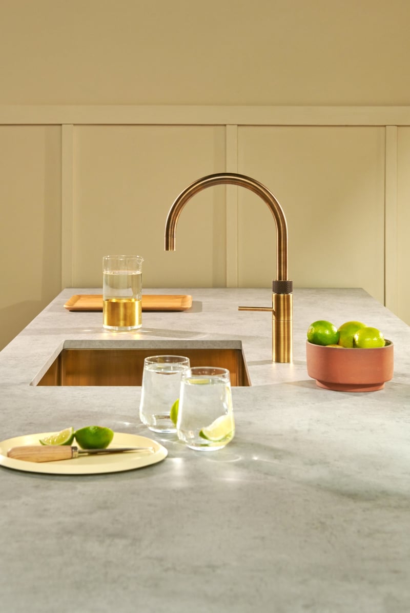 Quooker Fusion Round in patinated brass boiling water tap — with fresh lime, editorial still life in a real customer kitchen. Genuine Quooker product supplied by Watertap.eu.