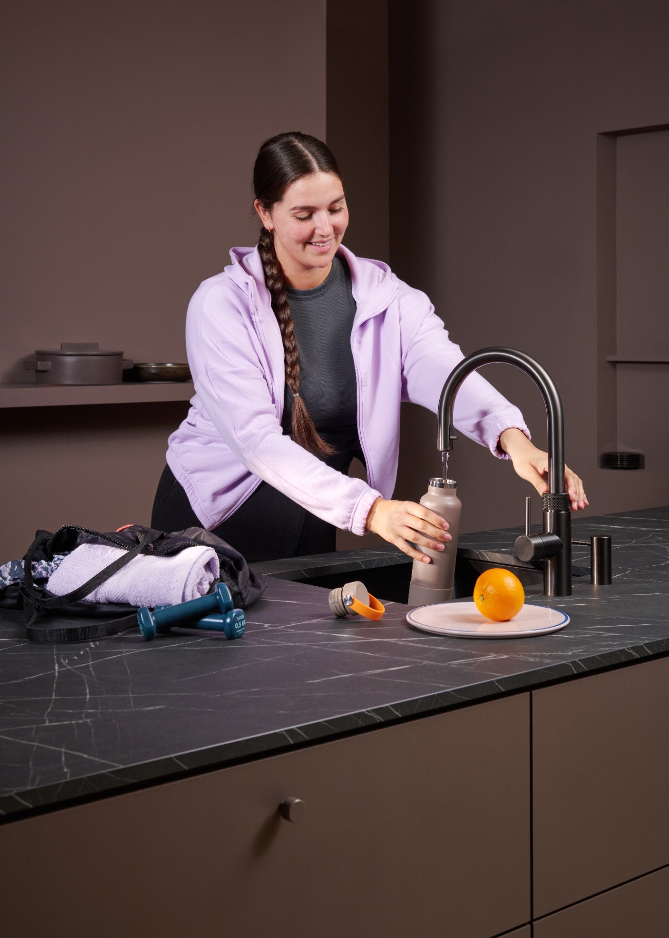 Woman filling a sports bottle at a Flex Round gun metal Quooker after workout