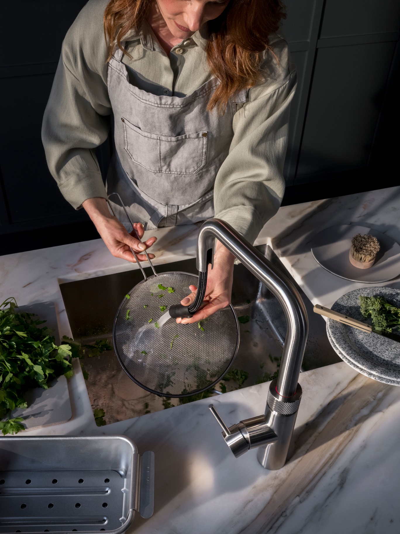 Overhead of a woman rinsing coriander in a strainer using the pull-out hose of a Flex Square stainless steel Quooker