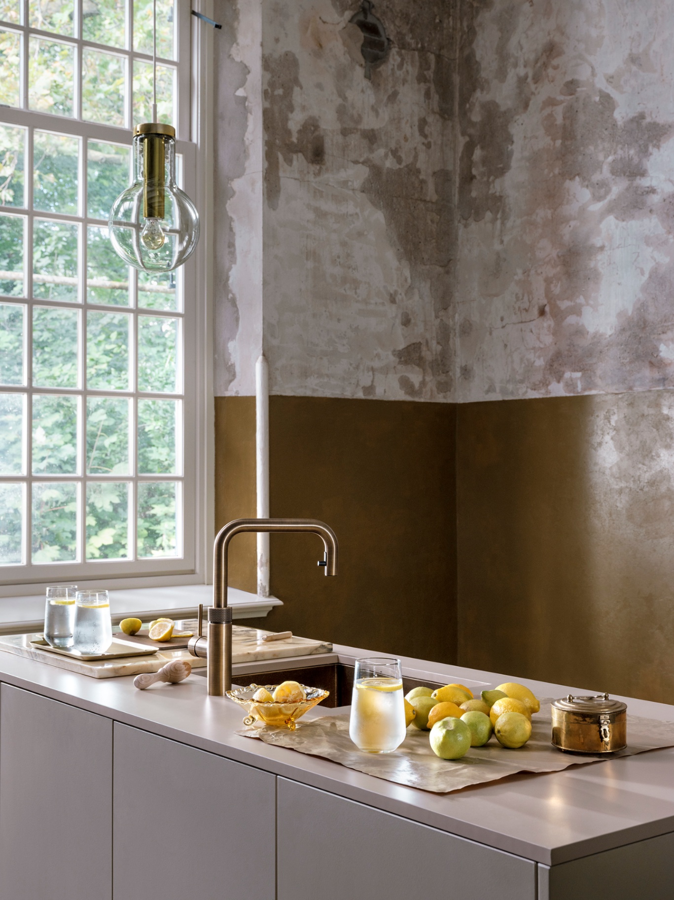 Editorial still of a Flex Square patinated brass Quooker with a spread of lemons on a light stone worktop