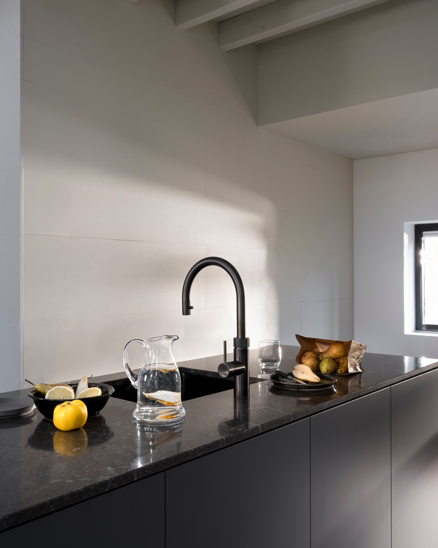 Editorial still of a Flex Round gun metal Quooker with a lemon-infused water carafe on a black marble worktop