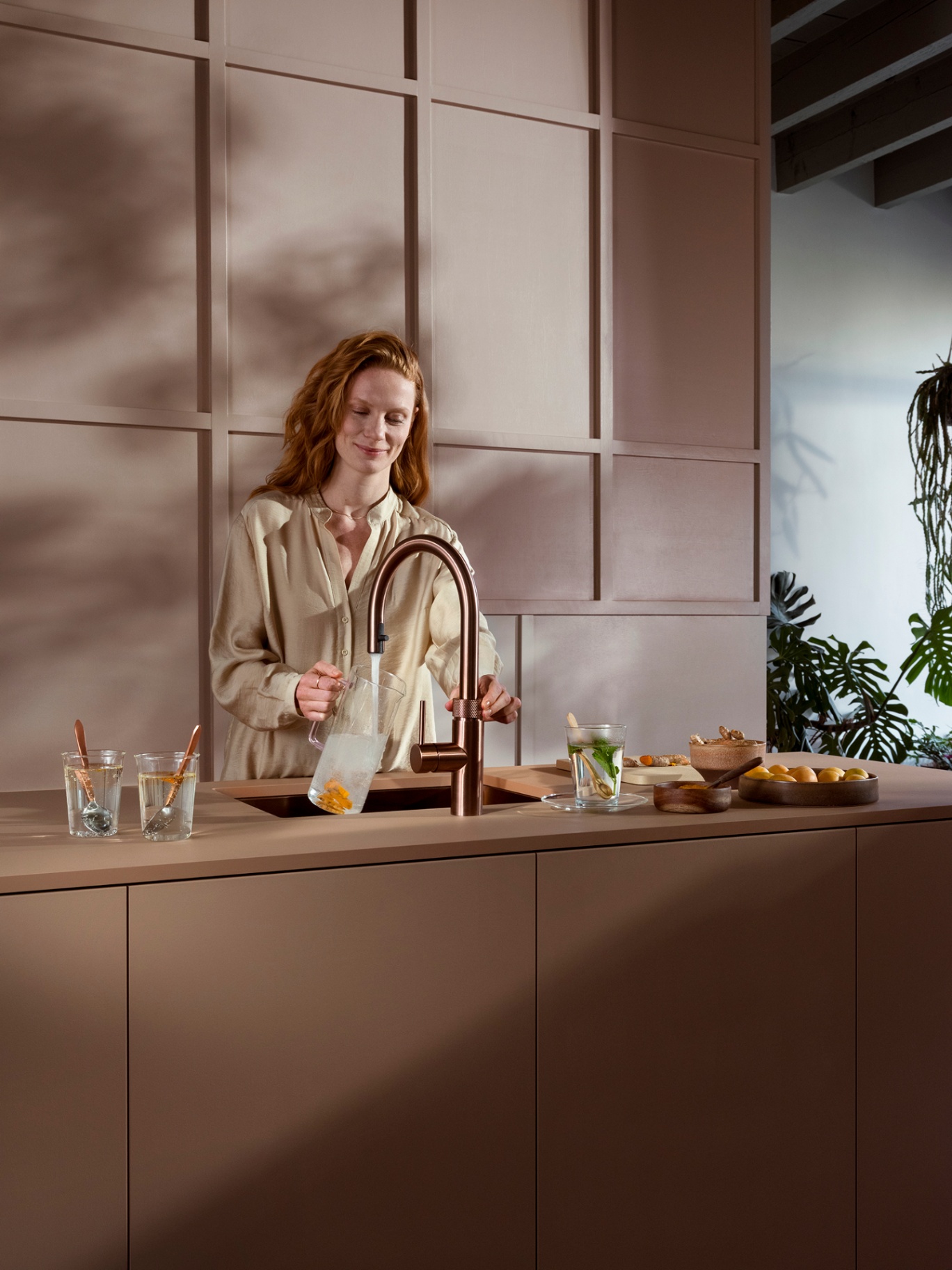 Woman pouring apricot-infused sparkling water from a Flex Round rose copper Quooker in a blush panelled kitchen