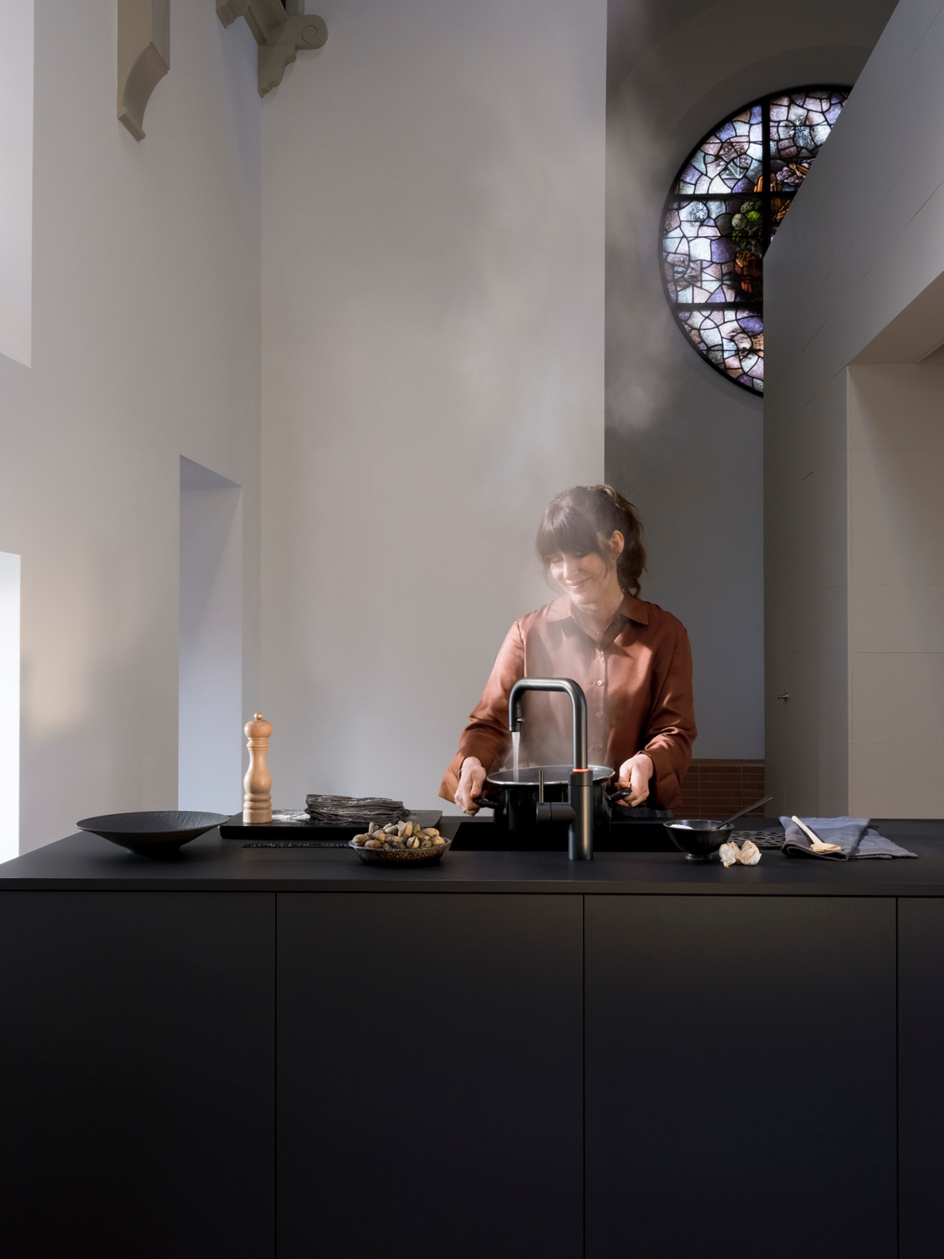 Woman boiling a saucepan at a Flex Square black Quooker in a converted chapel kitchen with stained glass