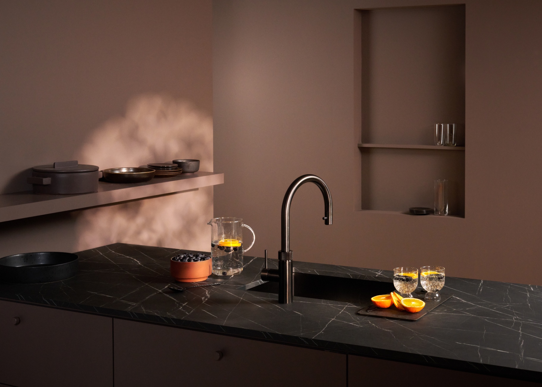 Editorial still of a Flex Round gun metal Quooker with sparkling fruit carafe on dark marble