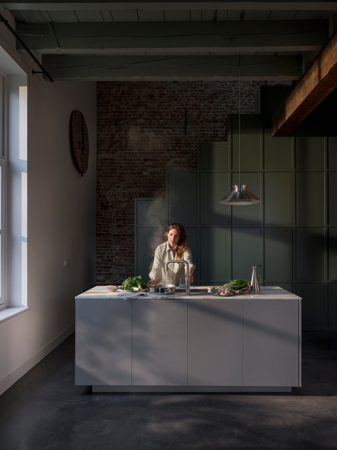 Woman boiling broccoli at a Flex Square stainless steel Quooker in a loft kitchen with brick and green panelling
