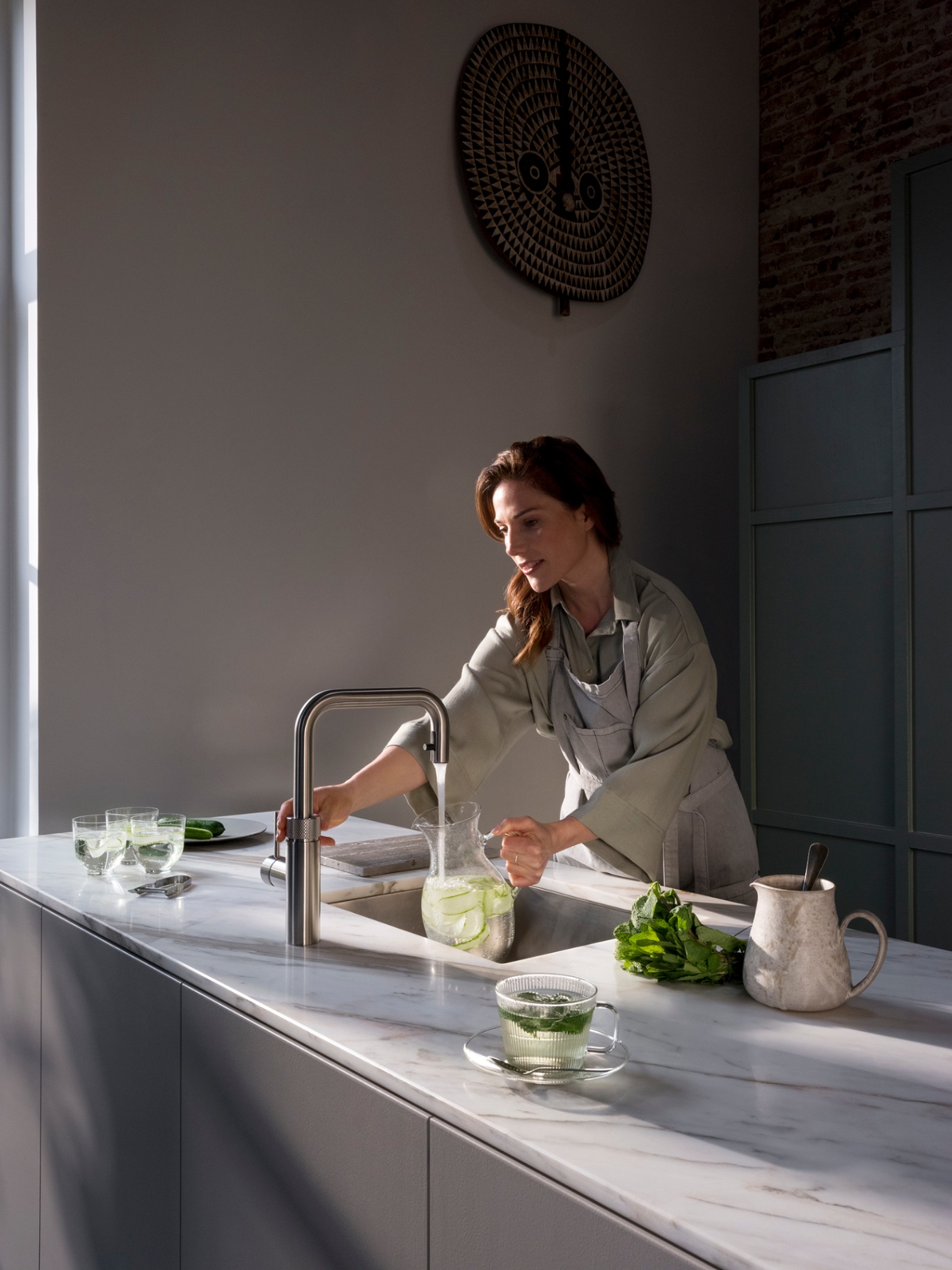 Woman pouring cucumber-mint sparkling water at a Flex Square stainless steel Quooker on Calacatta marble