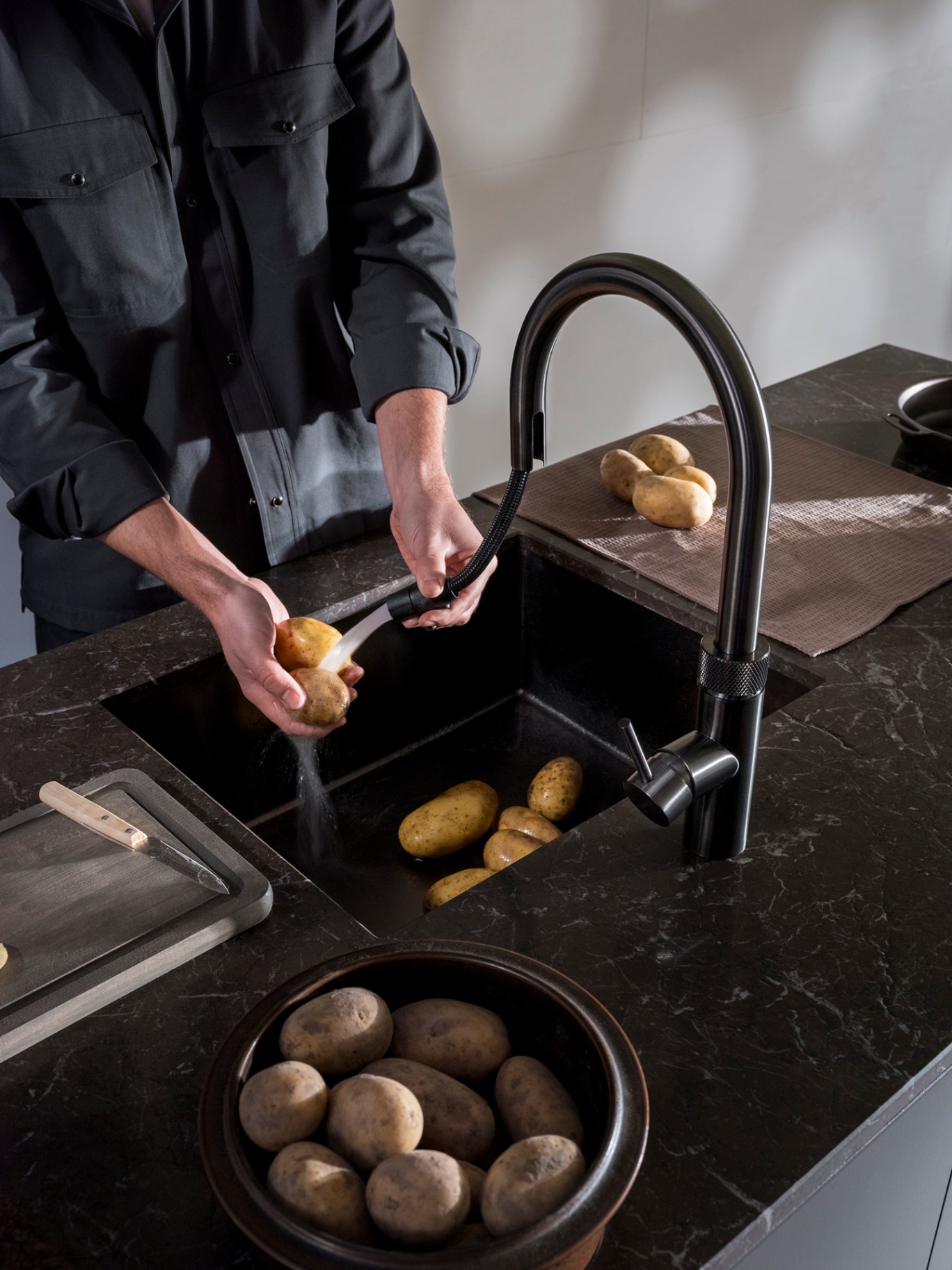Chef rinsing potatoes with the pull-out hose of a Flex Round gun metal Quooker on dark marble