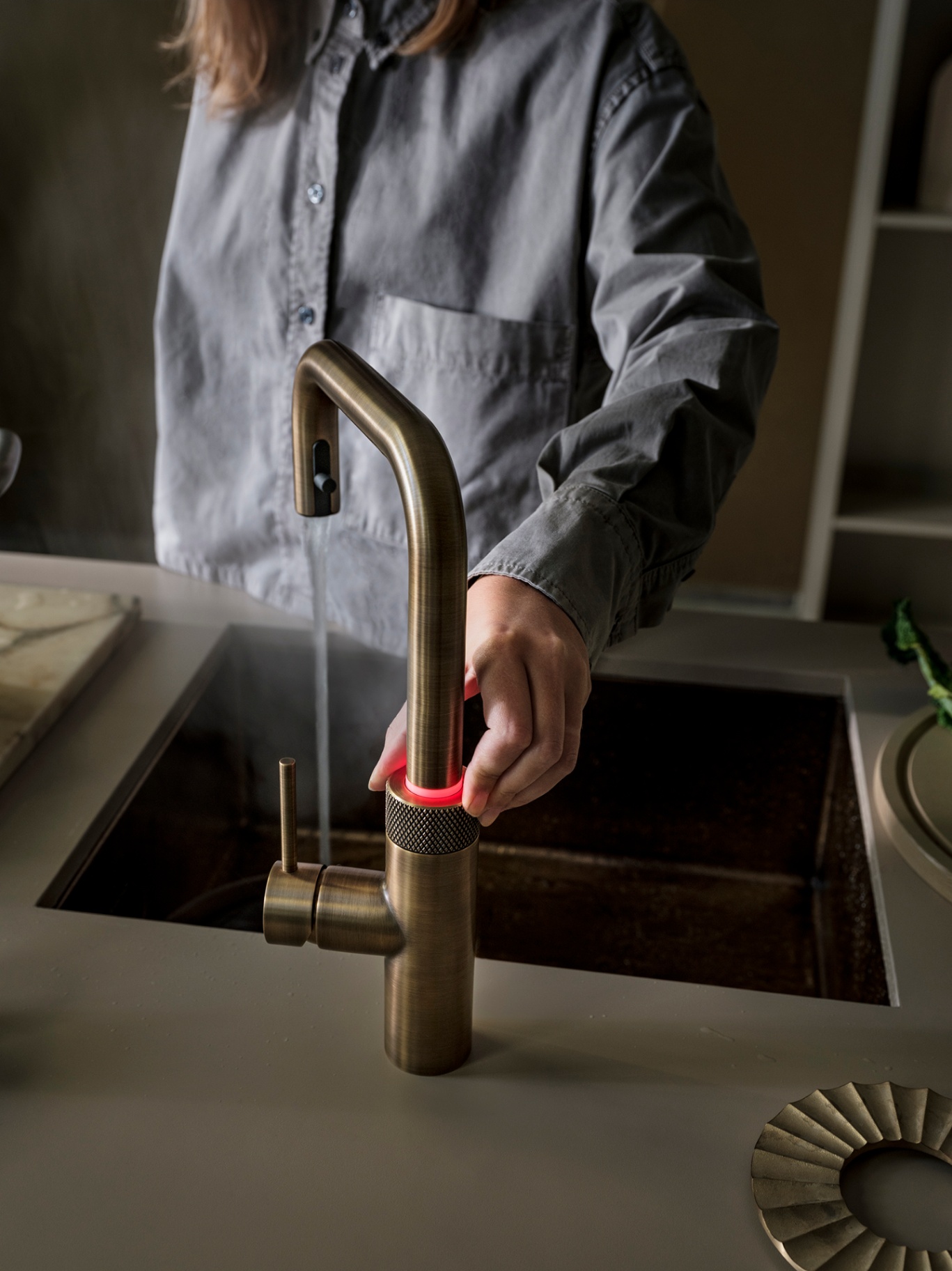 Close-up of a Flex Square patinated brass Quooker dispensing boiling water with red LED safety ring lit