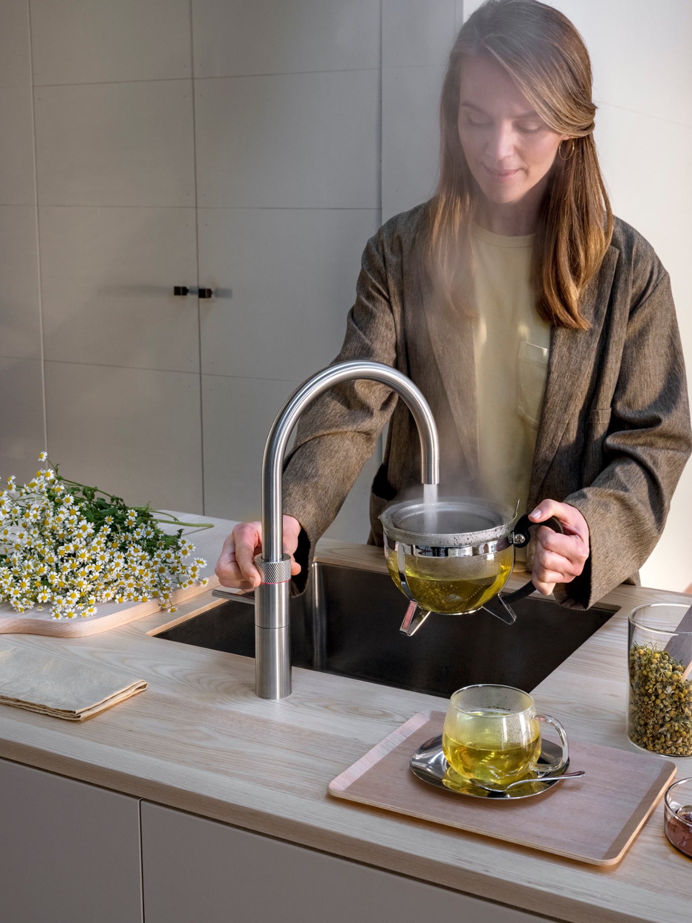 Woman brewing chamomile tea beneath a Fusion Round stainless steel Quooker — close-up editorial