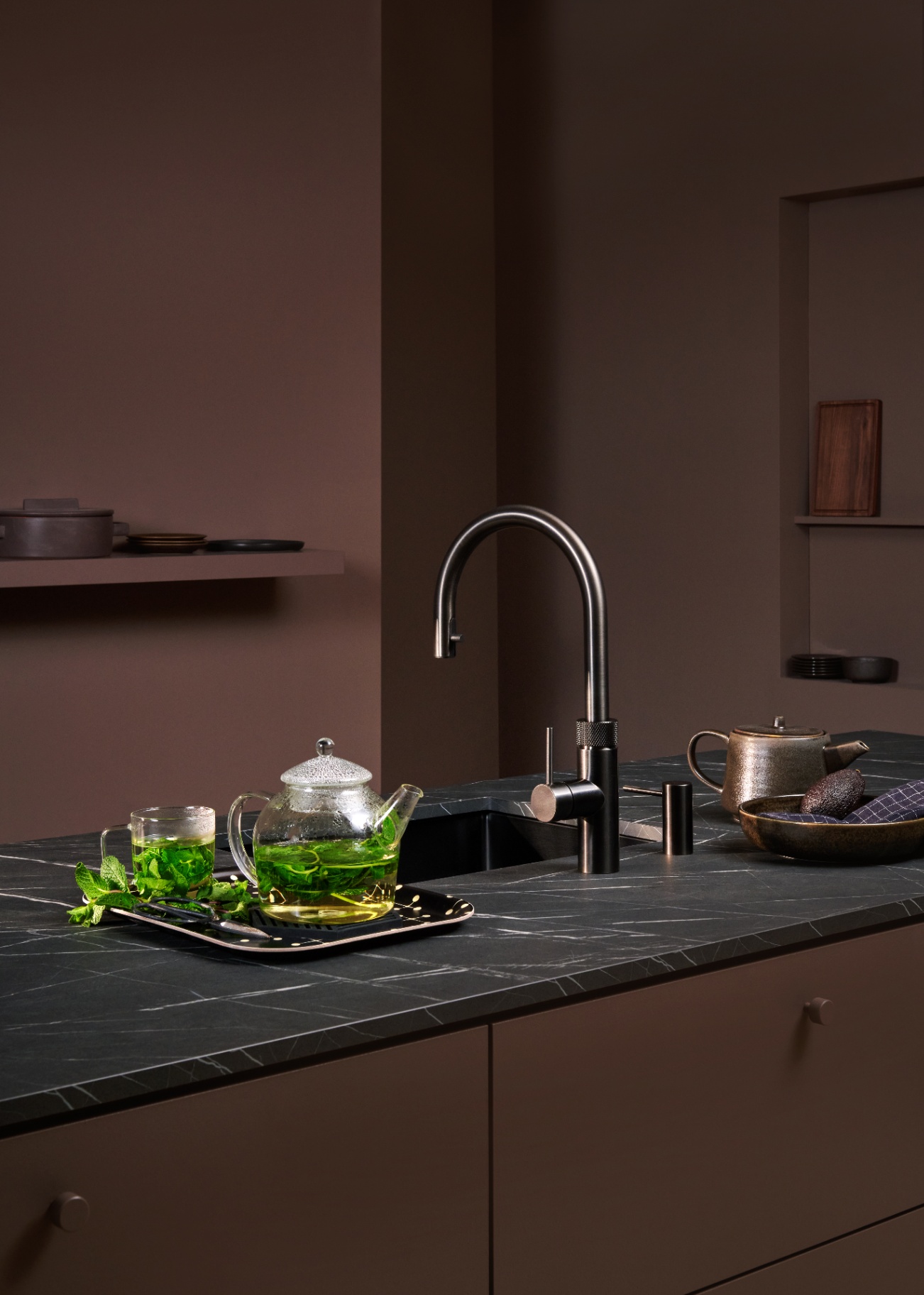 Still life of a Flex Round gun metal Quooker with a glass teapot of fresh mint tea in a moody kitchen