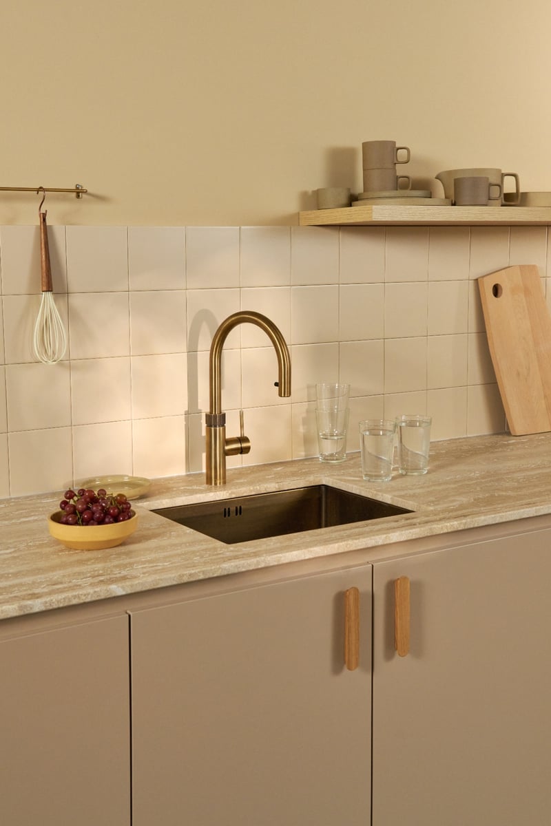 Quooker Flex Round in brass boiling water tap — in a warm beige kitchen, editorial still life in a real customer kitchen. Genuine Quooker product supplied by Watertap.eu.