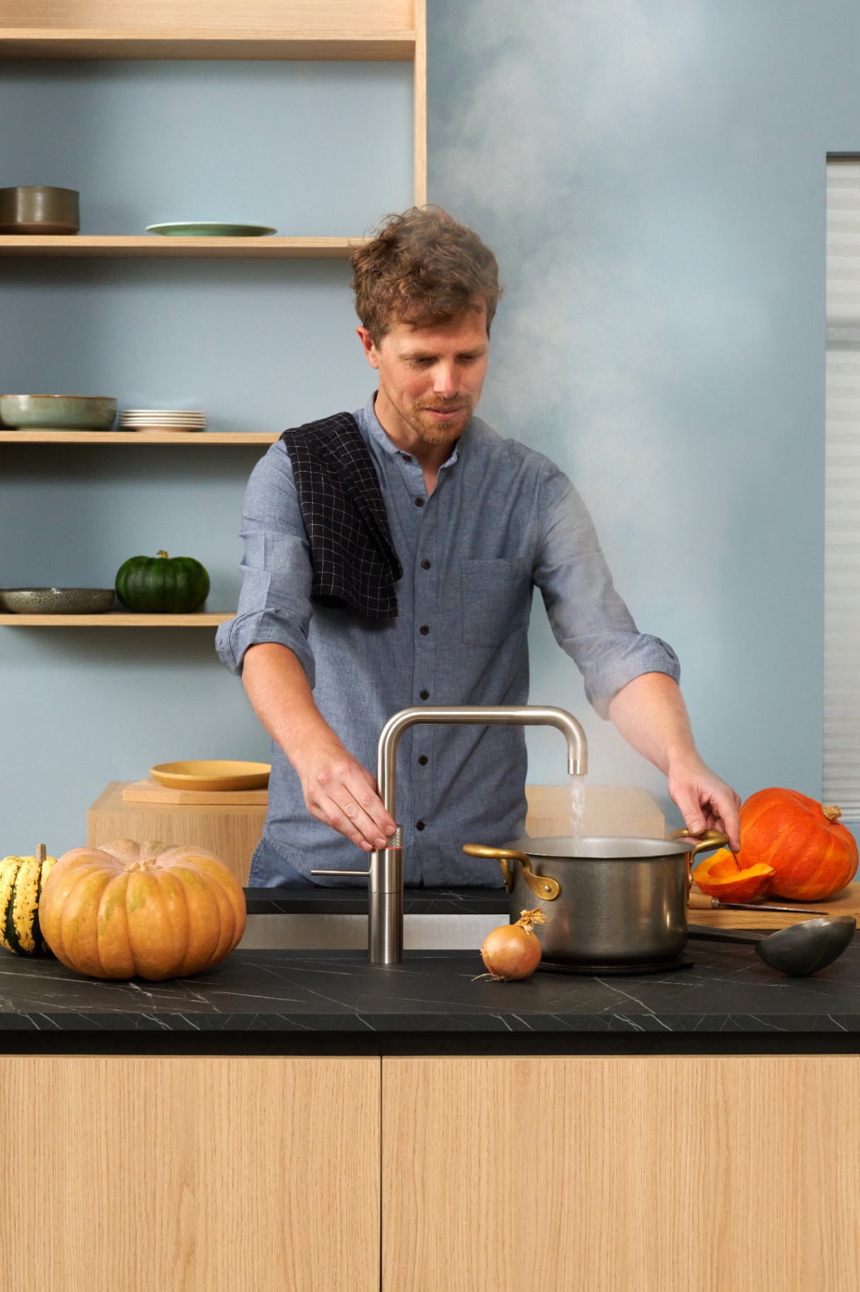 Chef boiling pumpkin soup below a Fusion Square stainless steel Quooker in a blue kitchen