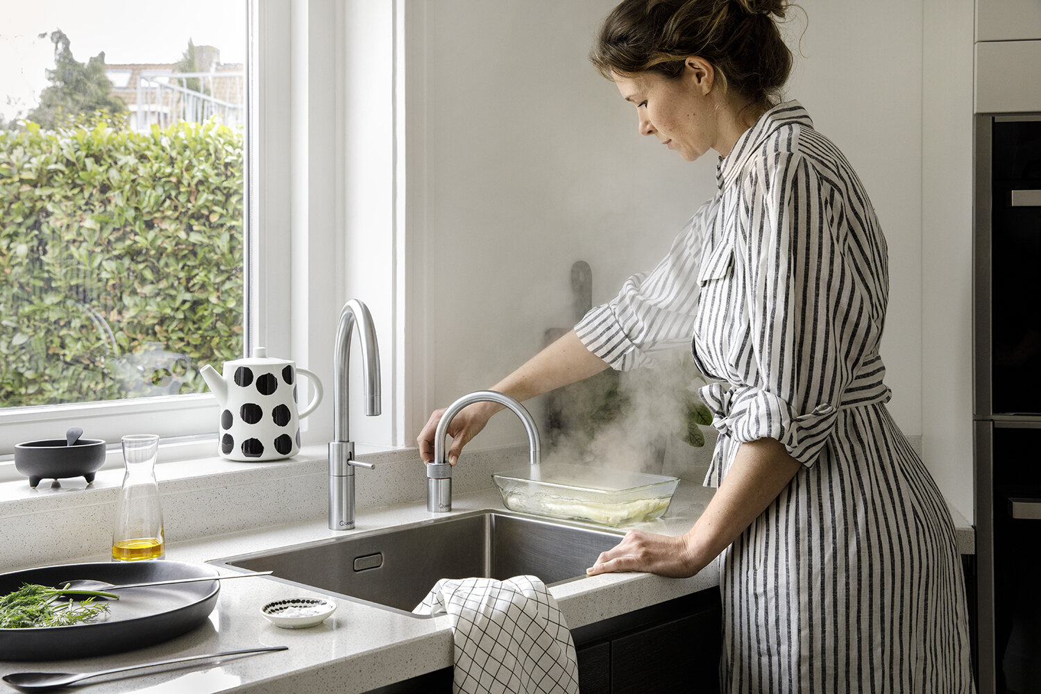 Woman poaching fish at Nordic Twin taps in stainless steel by a garden window