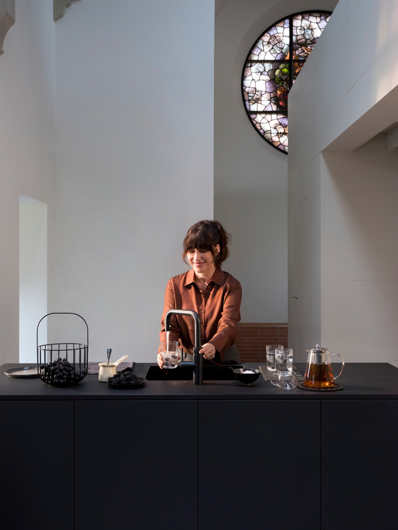 Woman filling a glass with sparkling water and blackberries at a Flex Square black Quooker