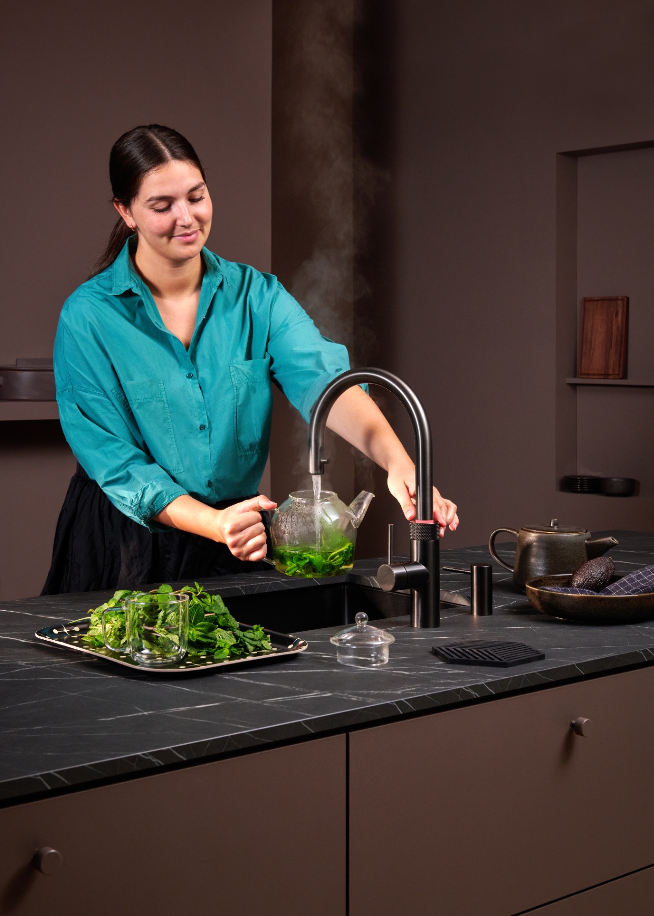 Woman brewing fresh mint tea at a Flex Round gun metal Quooker in a moody kitchen
