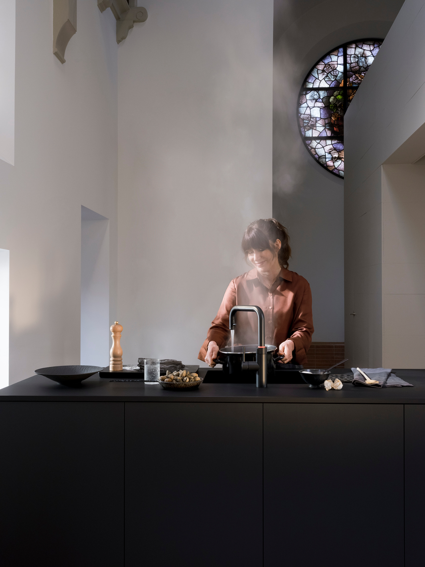 Woman cooking clams at a Flex Square black Quooker in a cathedral kitchen with stained glass