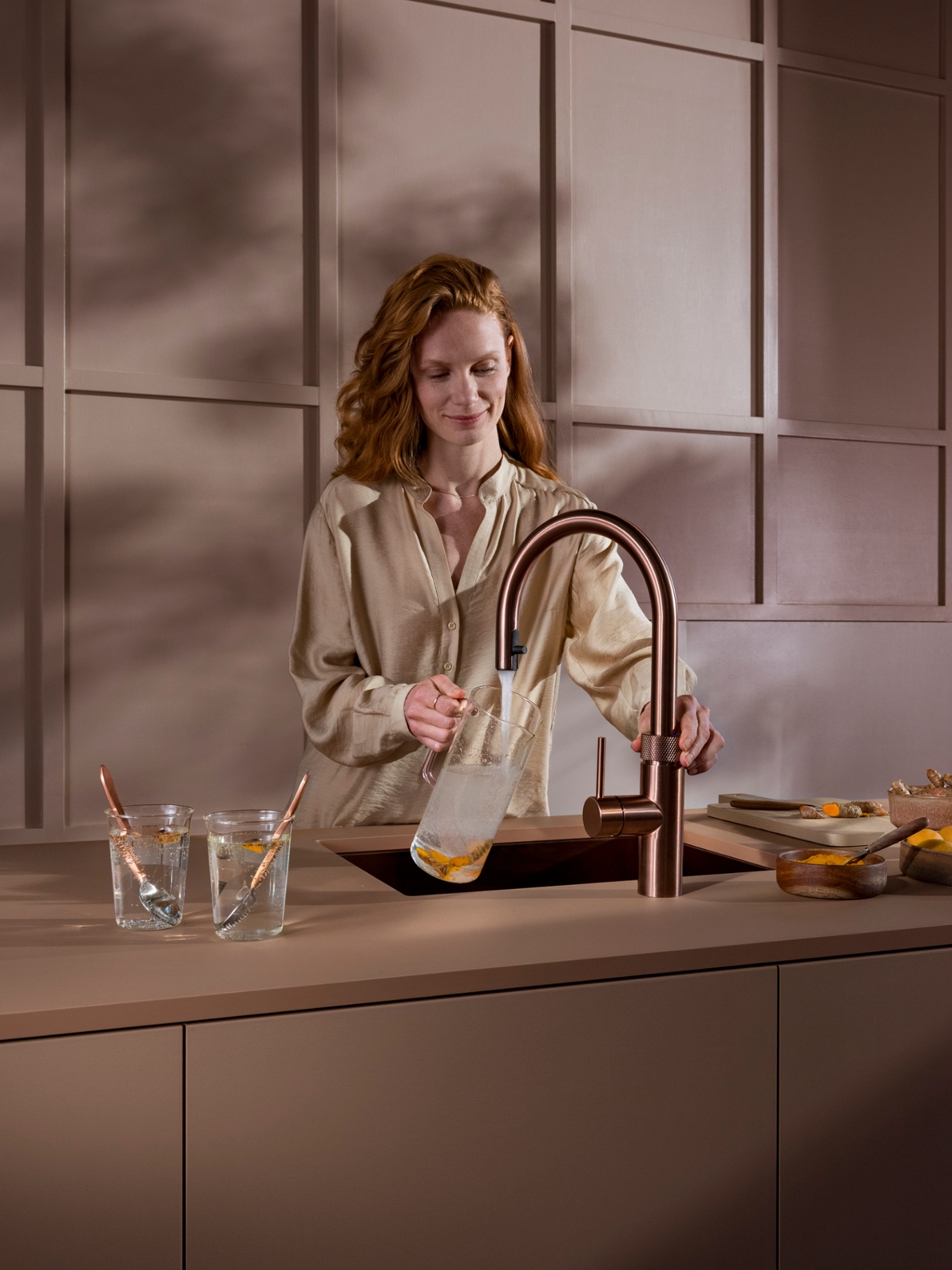 Woman filling a carafe of turmeric-infused sparkling water at a Flex Round rose copper Quooker