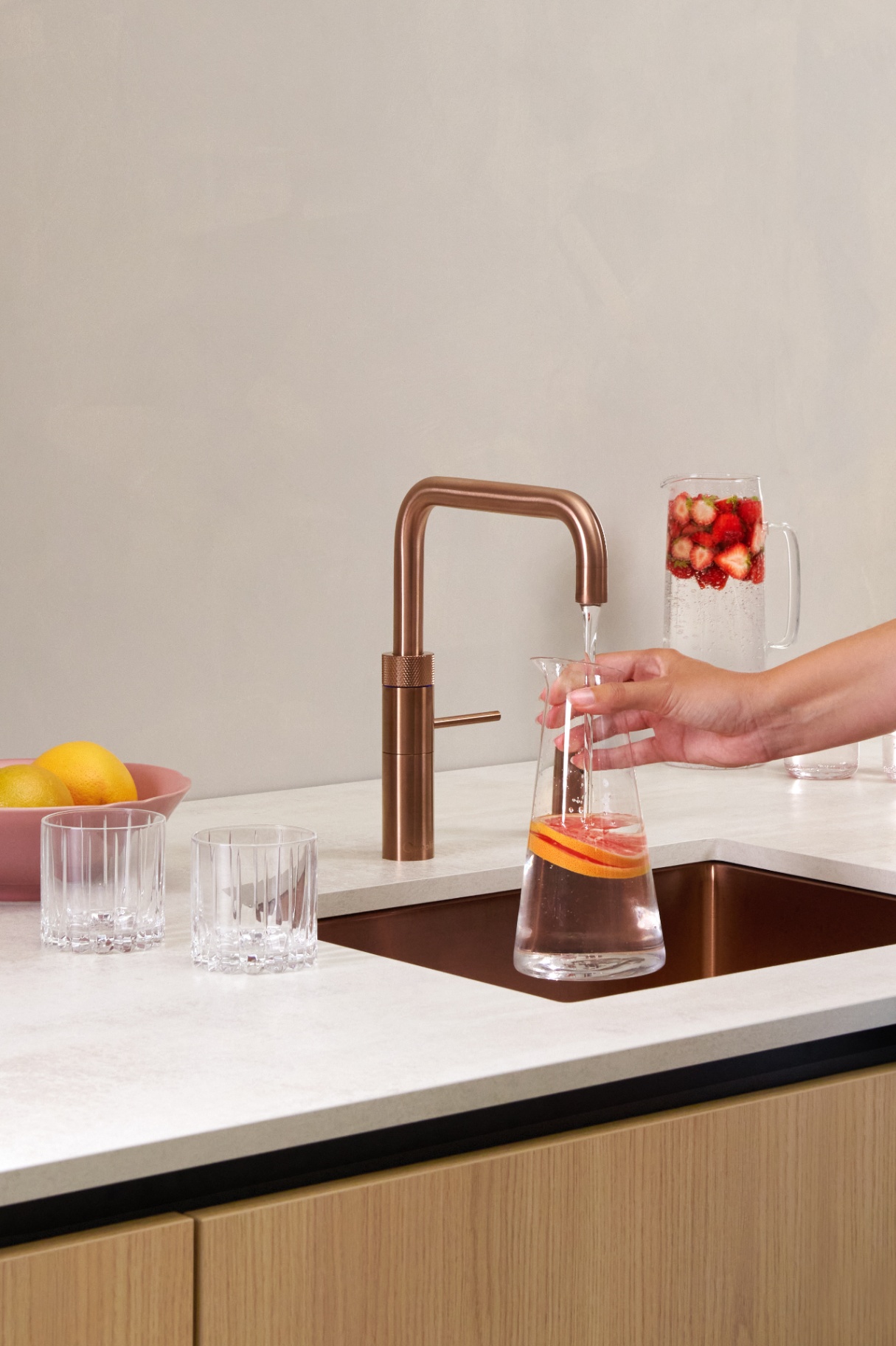 Woman pouring grapefruit-infused water from a Fusion Square rose copper Quooker