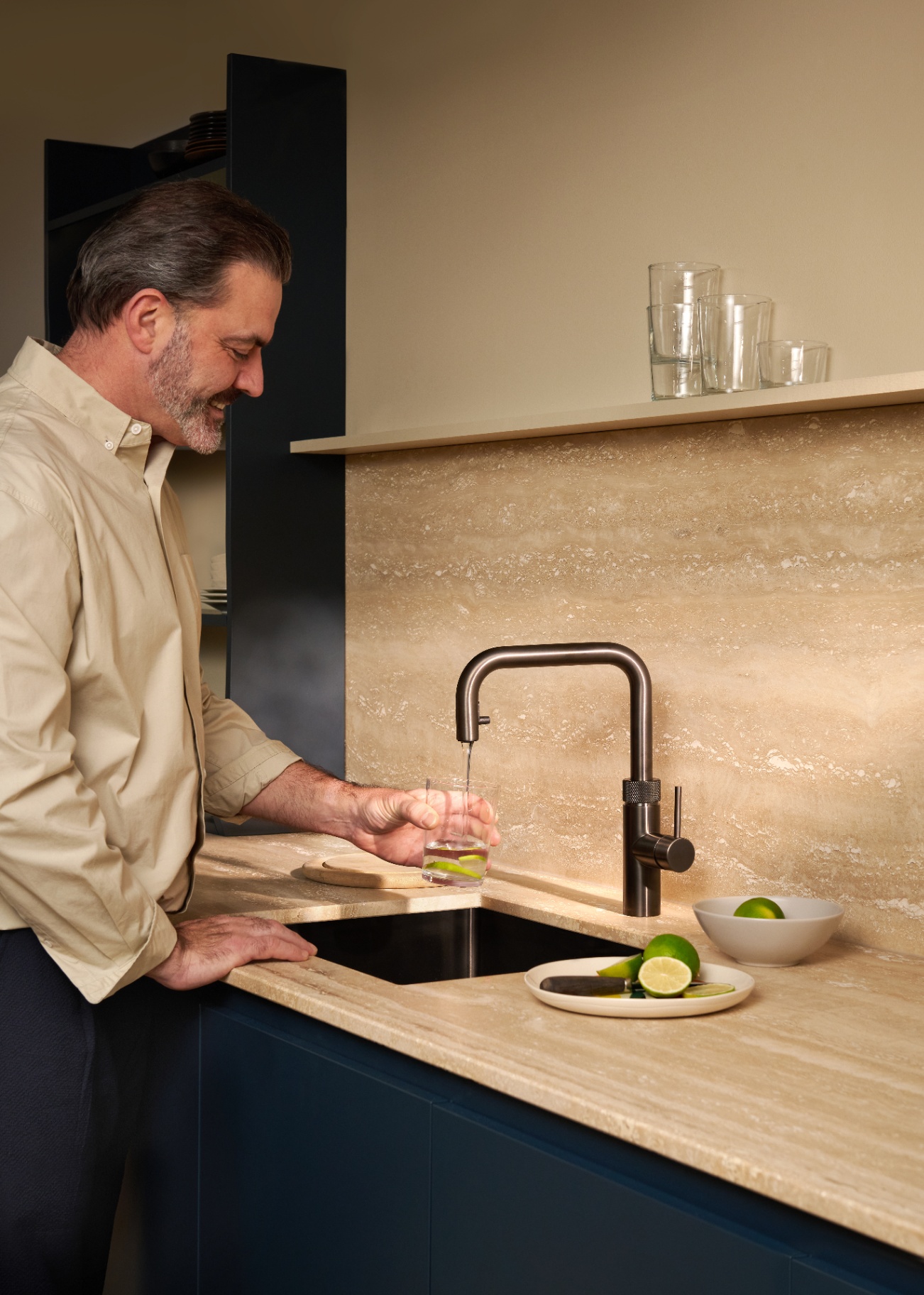 Man filling a lime-infused water glass at a Flex Square gun metal Quooker on travertine
