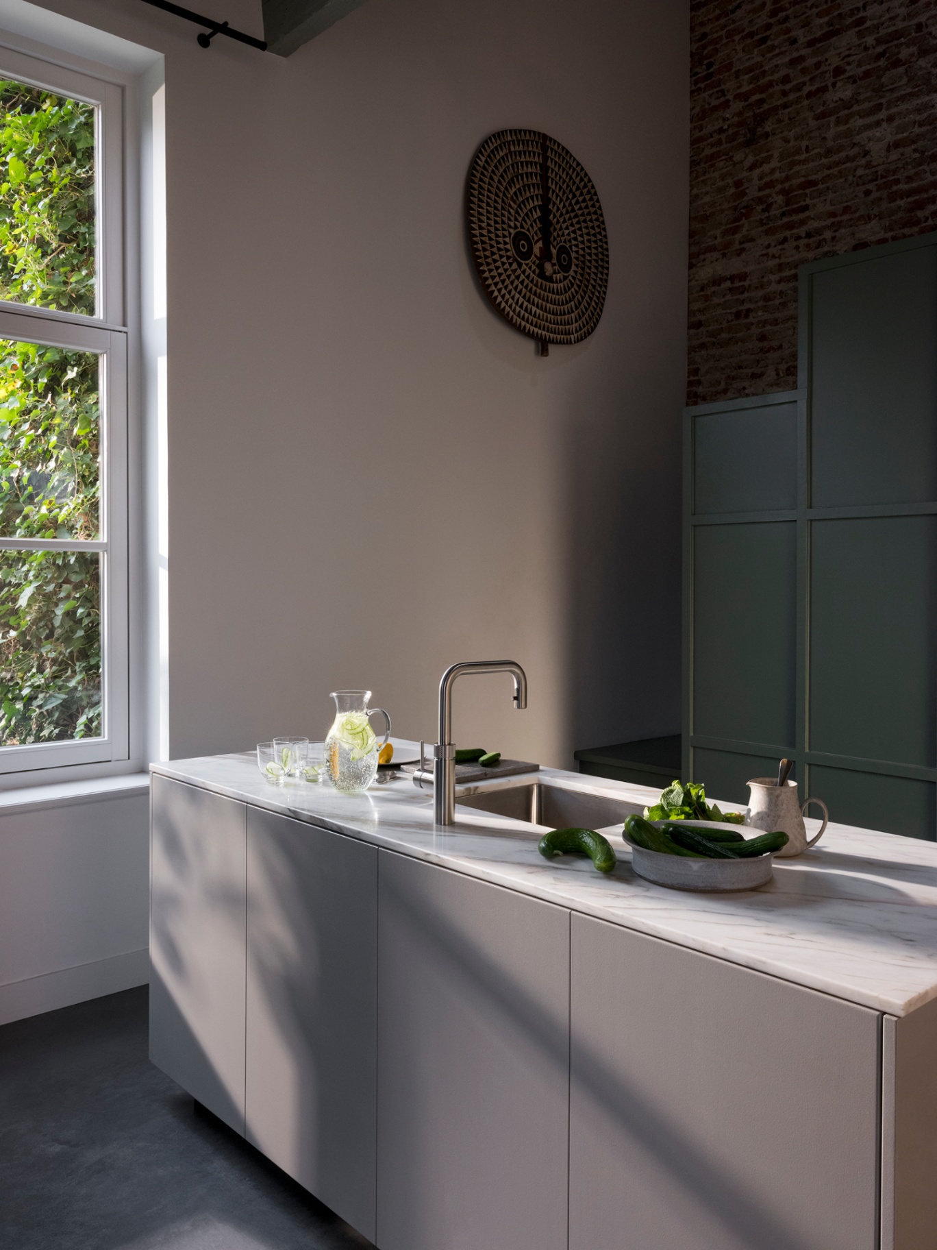 Editorial still of a Flex Square stainless steel Quooker on Calacatta marble with cucumber-infused water in a loft kitchen