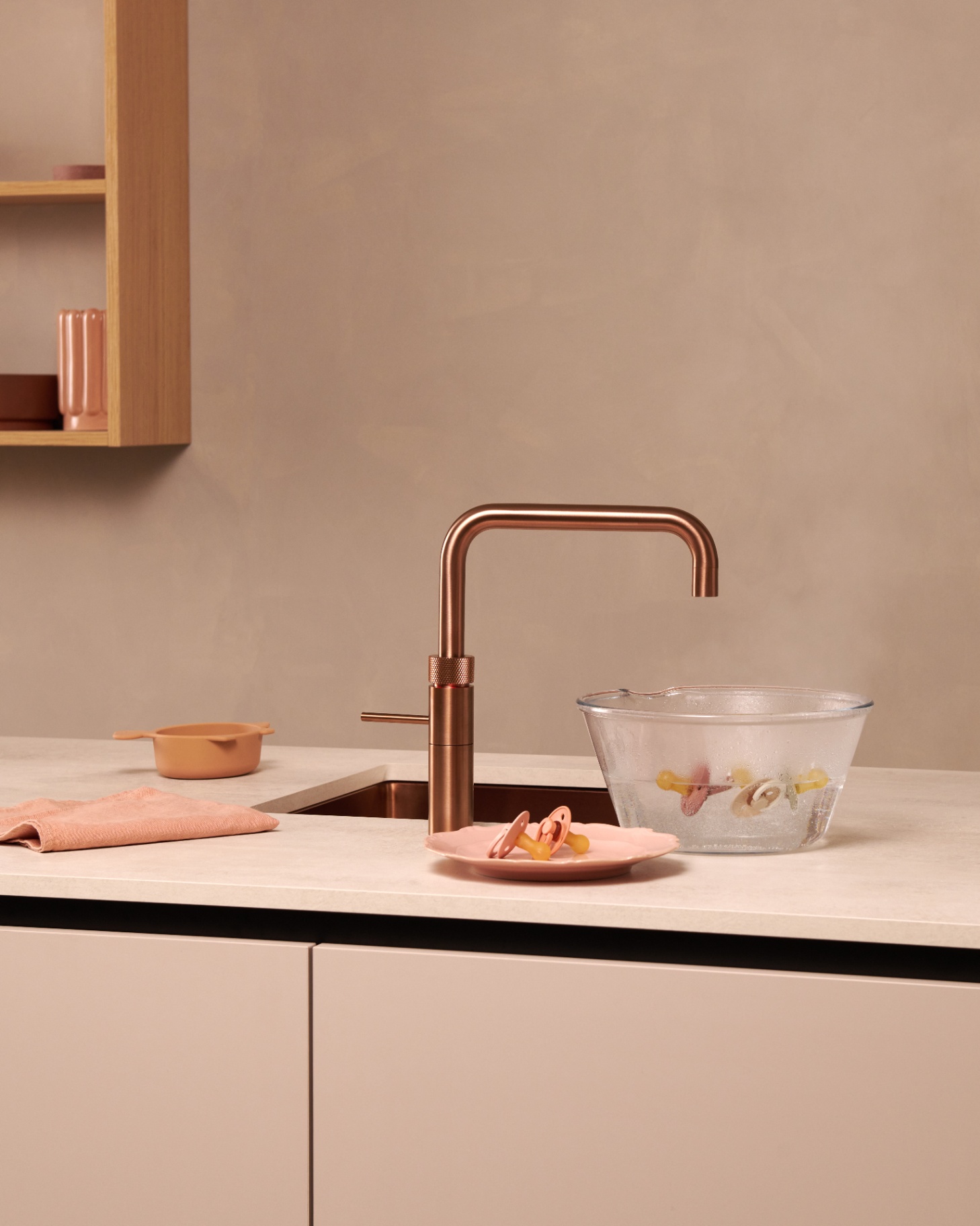Rose copper Fusion Square Quooker sanitising pacifiers in a glass bowl on a nude blush worktop