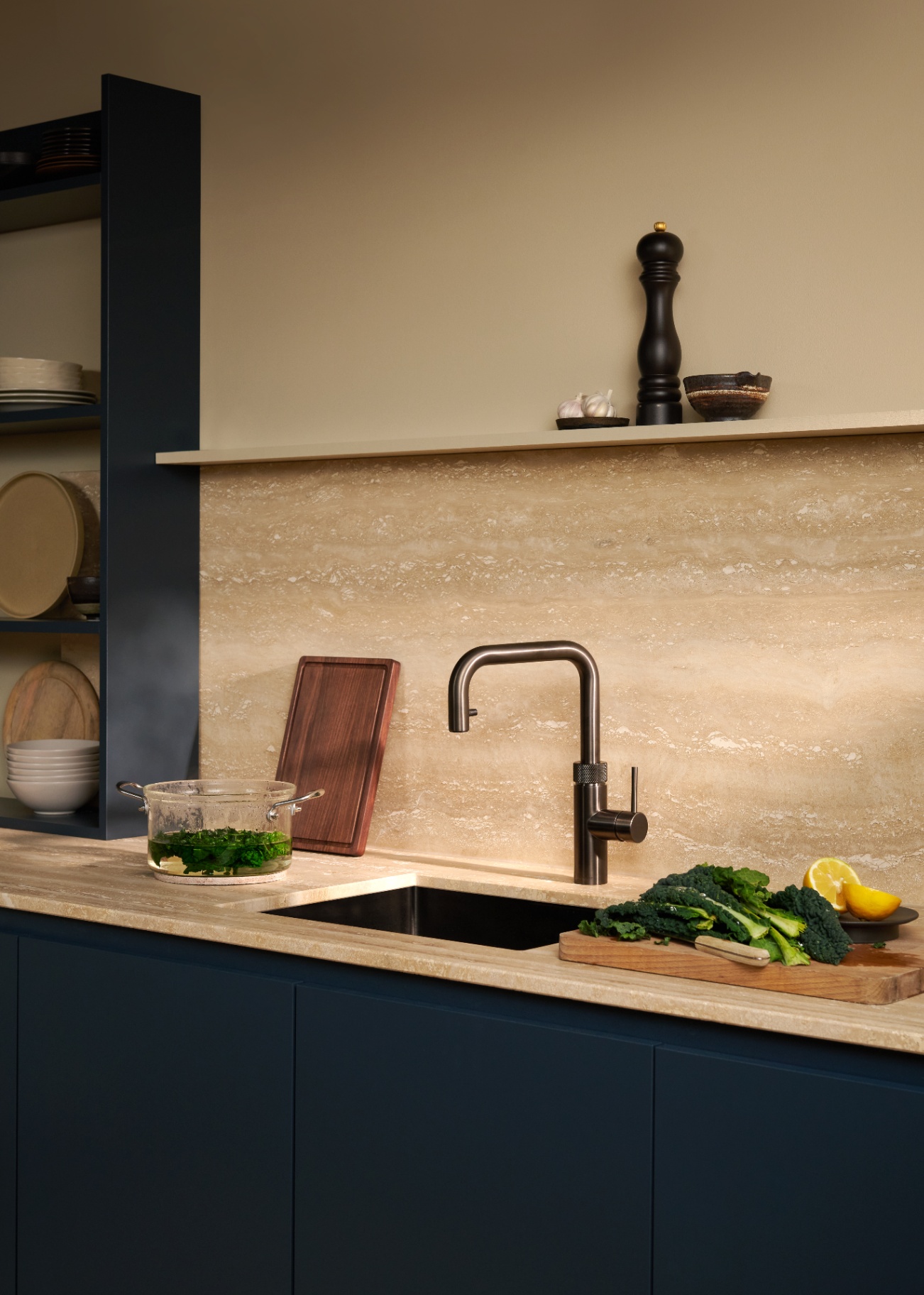 Editorial still life of a Flex Square gun metal Quooker on travertine with a glass pot of blanched greens