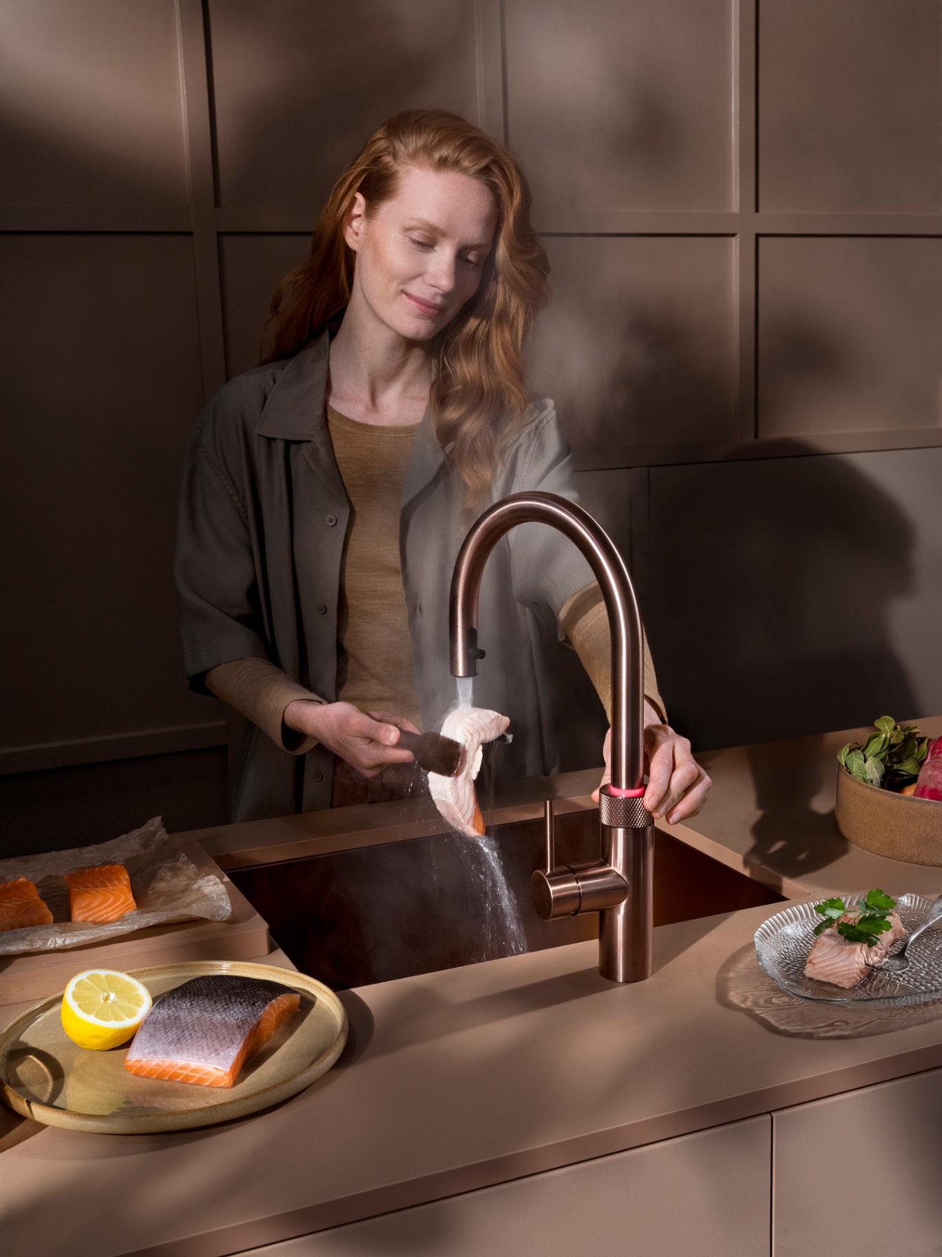 Close-up of a woman rinsing a salmon fillet at a Flex Round rose copper Quooker with red LED safety ring