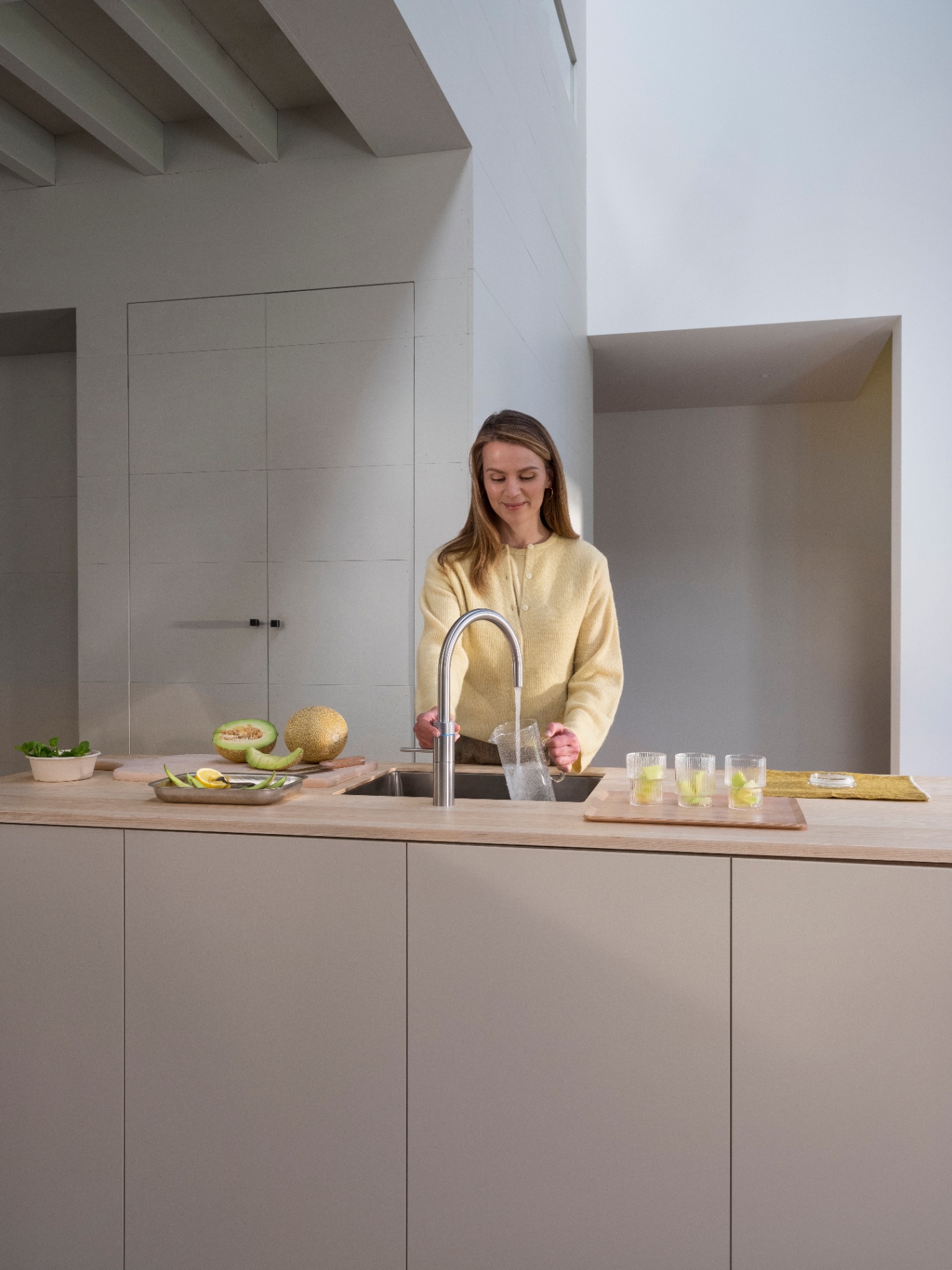 Woman pouring sparkling water into a carafe at a Fusion Round stainless steel Quooker in an architectural kitchen