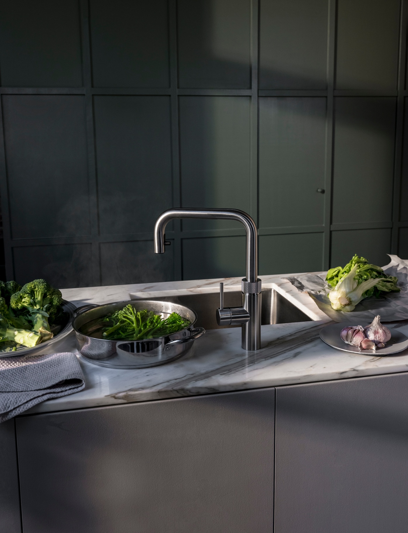 Editorial still of Flex Square stainless steel Quooker with steaming broccoli pan on marble