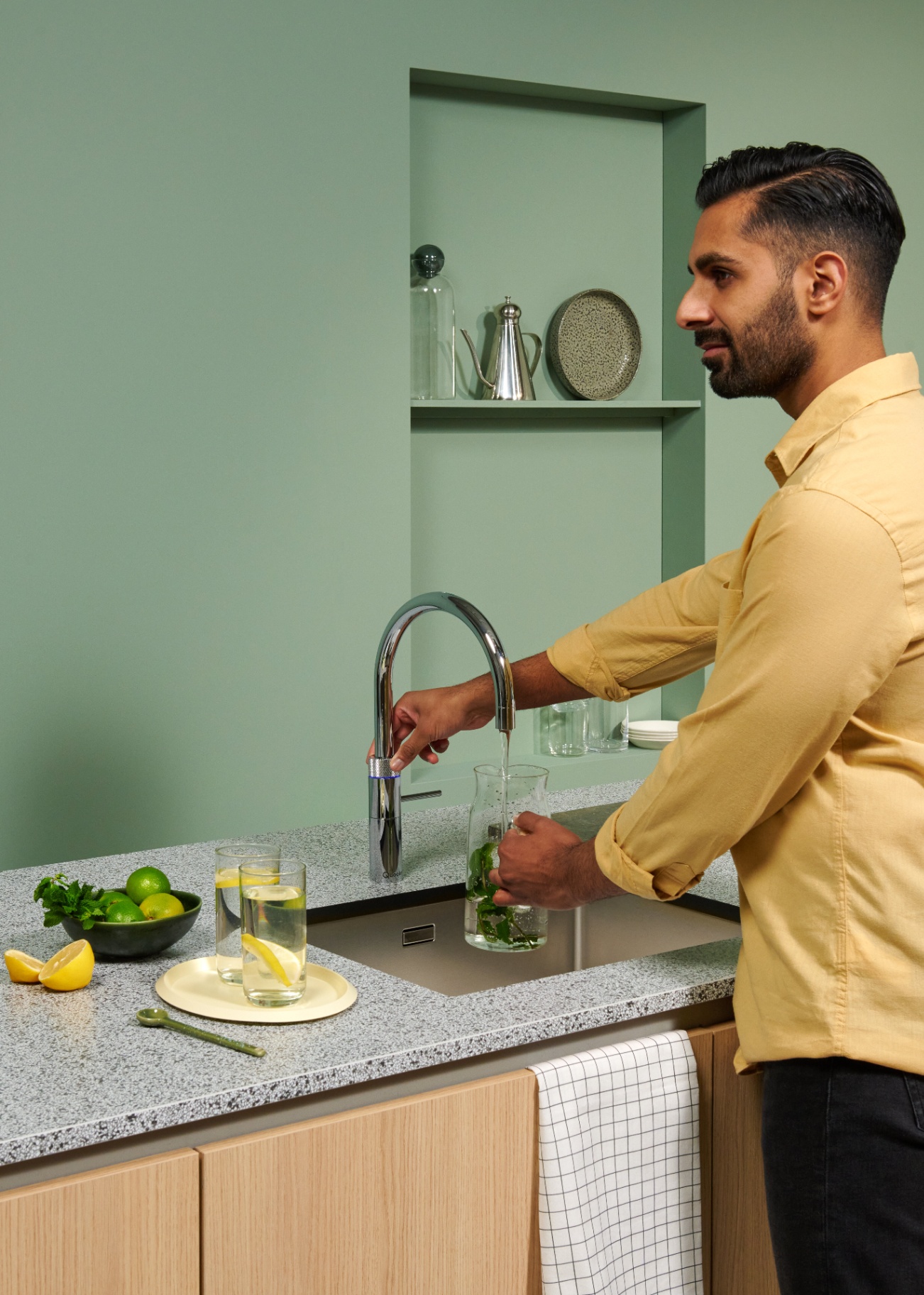 Man muddling mint in a carafe under a Fusion Round chrome Quooker in a sage green kitchen