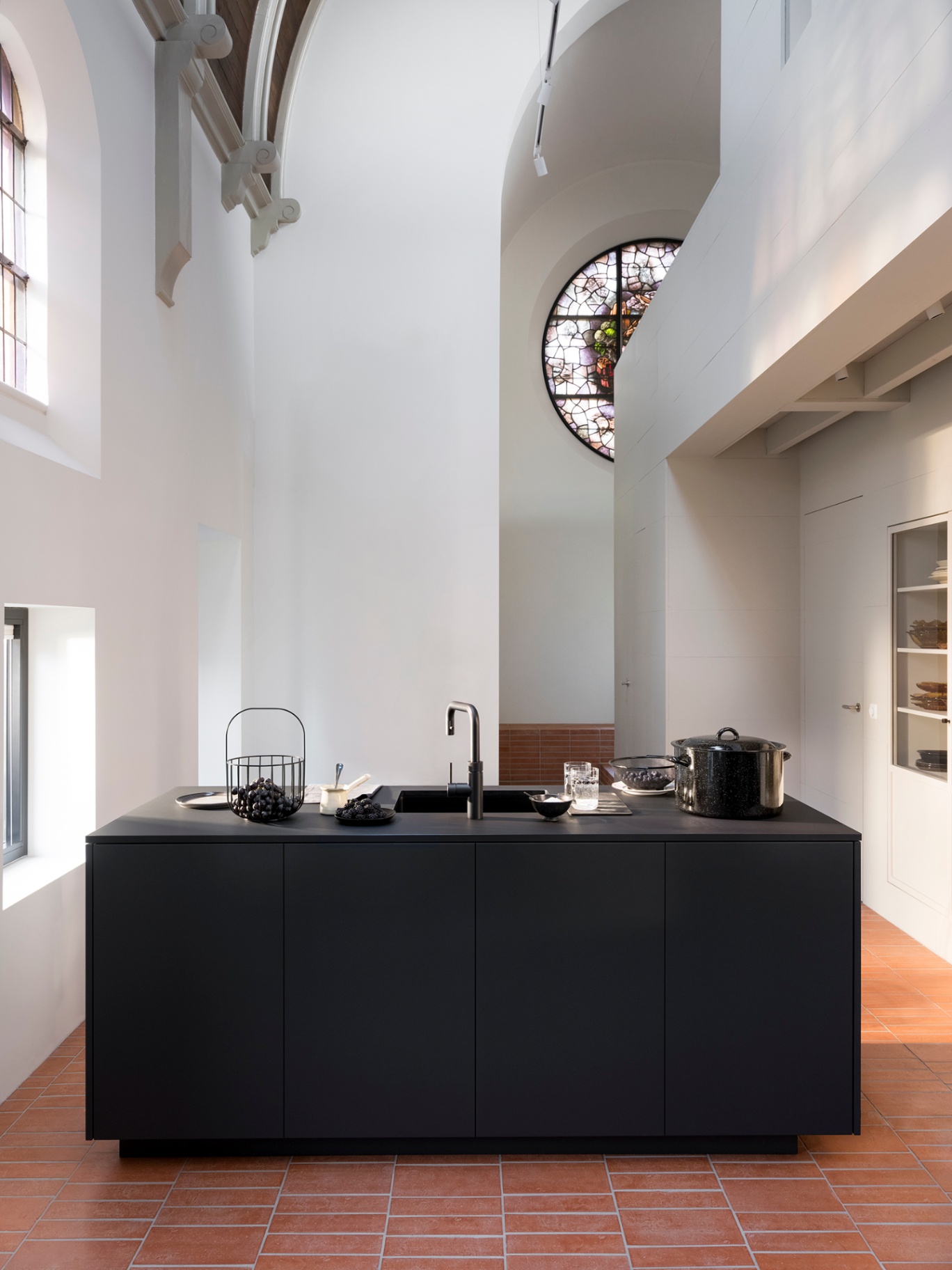 Wide architectural view of a Flex Square black Quooker island in a converted chapel with terracotta floor