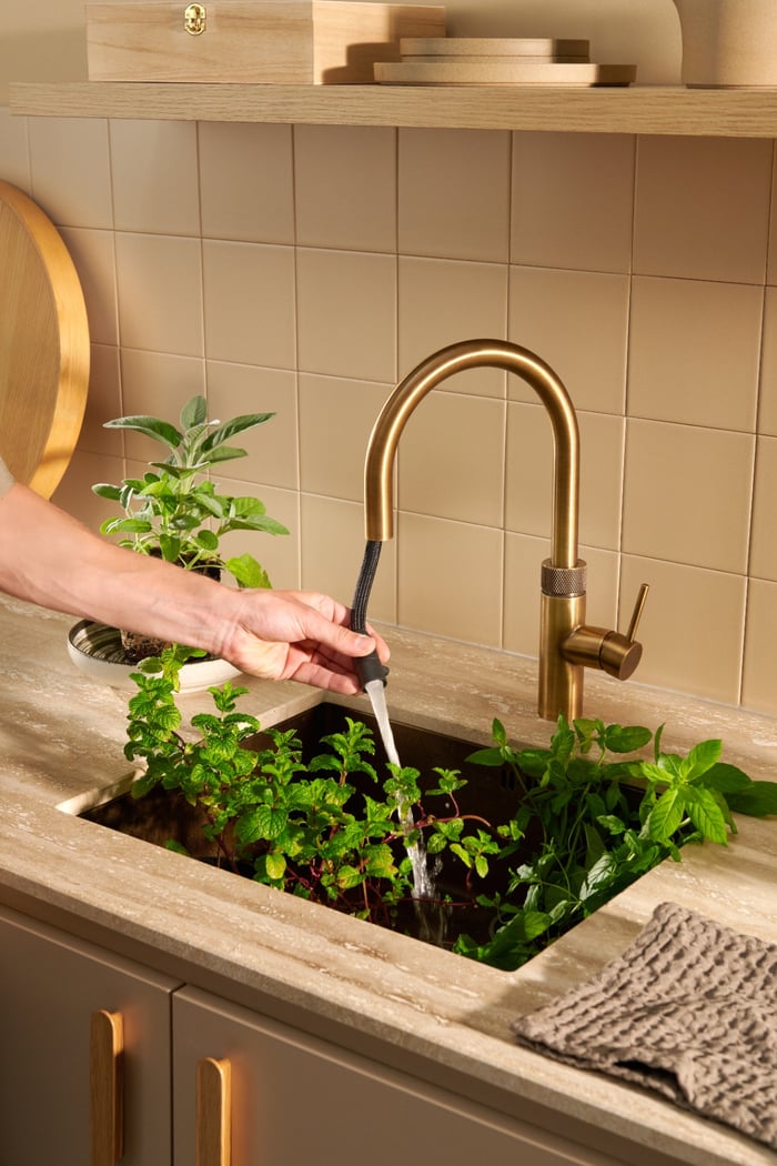Quooker Flex Round in patinated brass boiling water tap — rinsing fresh herbs in a real customer kitchen. Genuine Quooker product supplied by Watertap.eu.