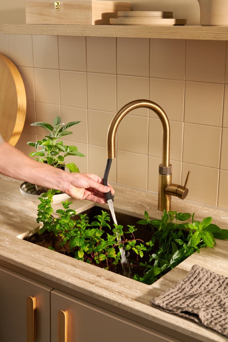 Quooker Flex Round in patinated brass boiling water tap — rinsing fresh herbs in a real customer kitchen. Genuine Quooker product supplied by Watertap.eu.