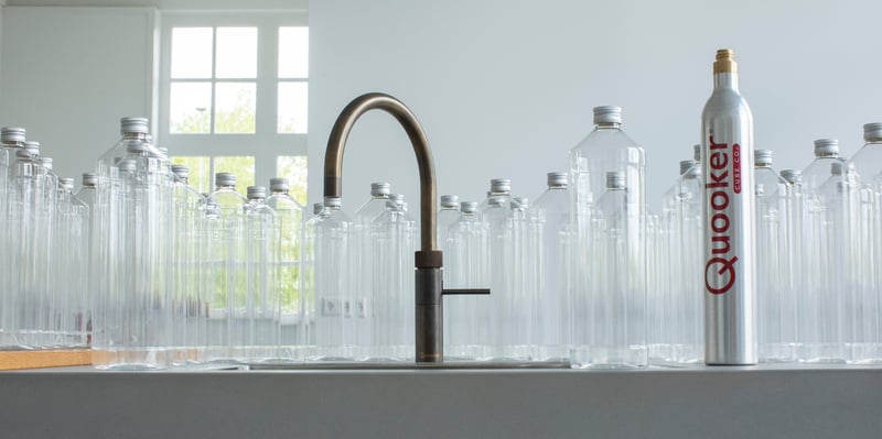 Quooker CUBE filtered chilled & sparkling system — 60-can capacity, empty bottles ready to refill, with empty bottles ready to refill, landscape composition in a real customer kitchen. Genuine Quooker product supplied by Watertap.eu.