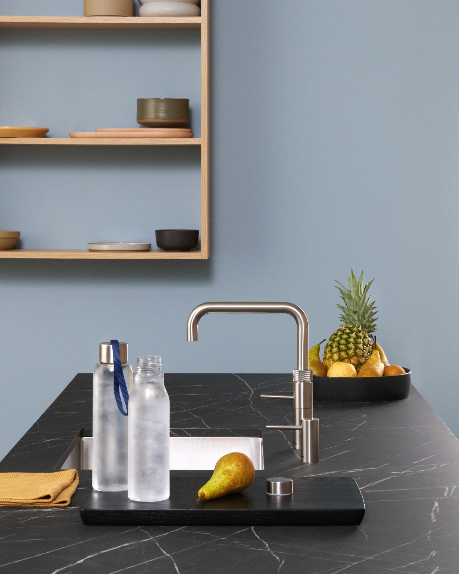 Still life of frosted bottles, pear and pineapple around a Fusion Square stainless steel Quooker on black marble