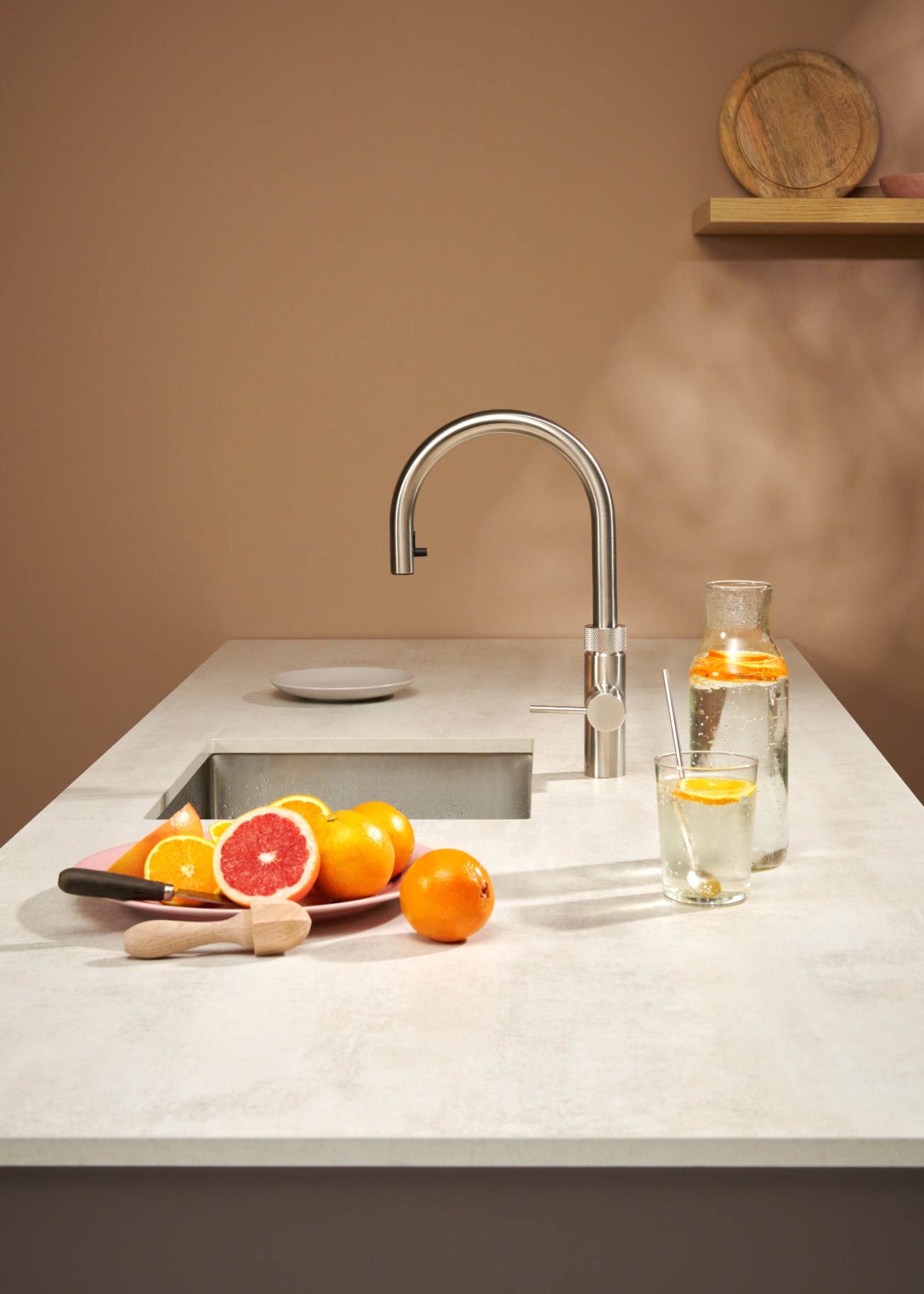 Flex Round 2.0 stainless steel Quooker with grapefruit carafe on a warm terracotta backdrop