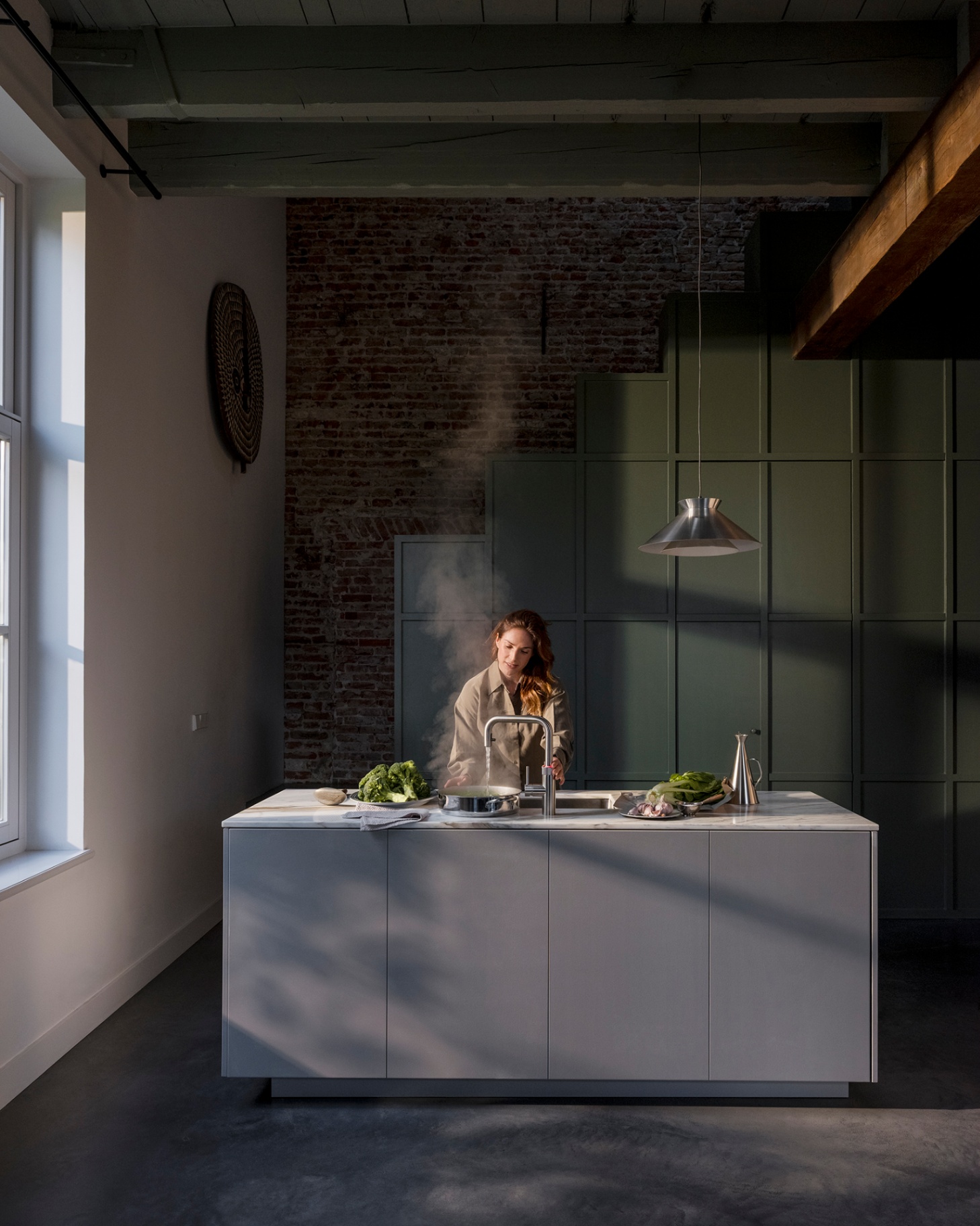 Woman boiling greens at a Flex Square stainless steel Quooker in a loft kitchen with exposed brick and green panelling