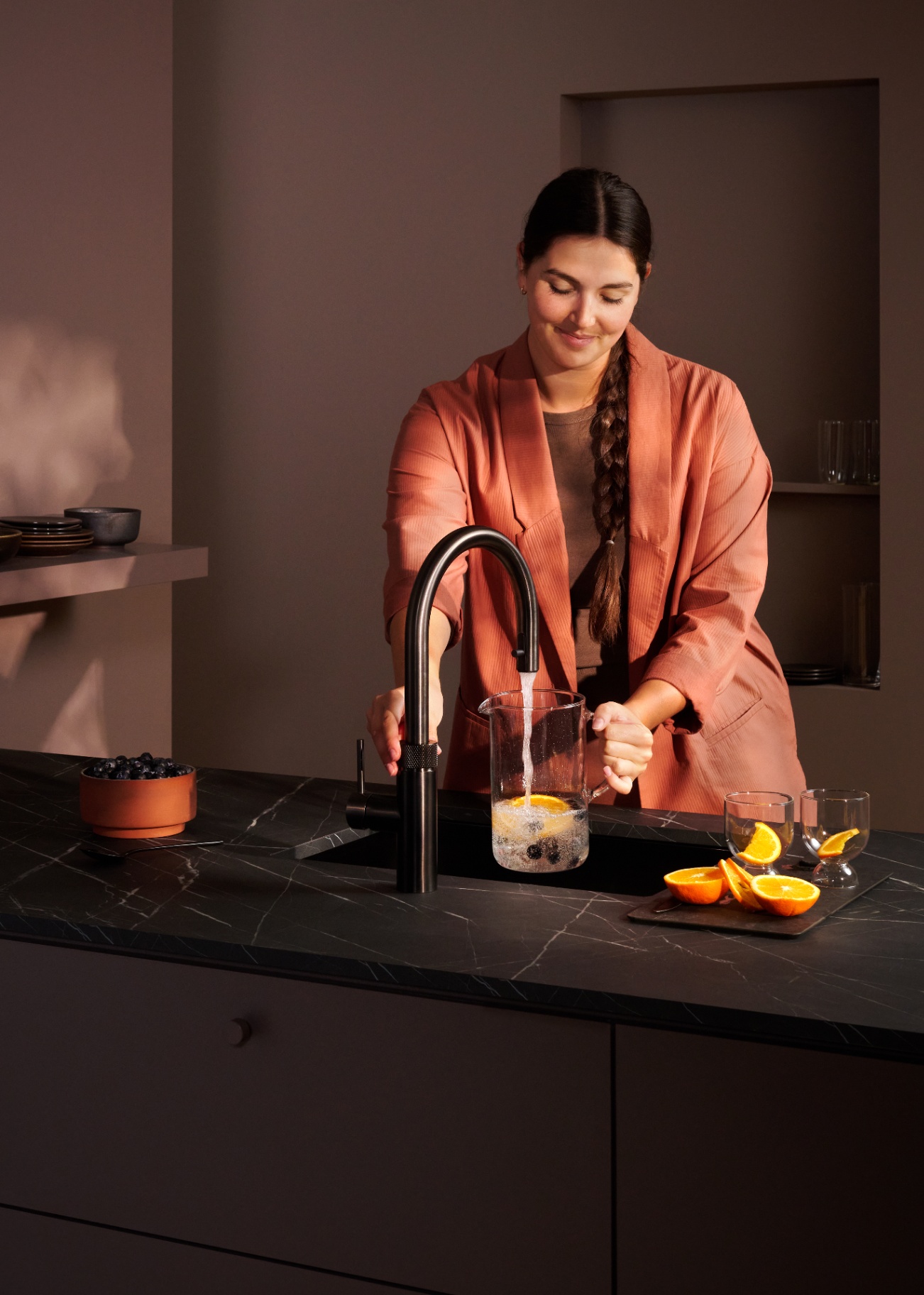 Woman filling a fruit-infused sparkling water carafe at a Flex Round gun metal Quooker