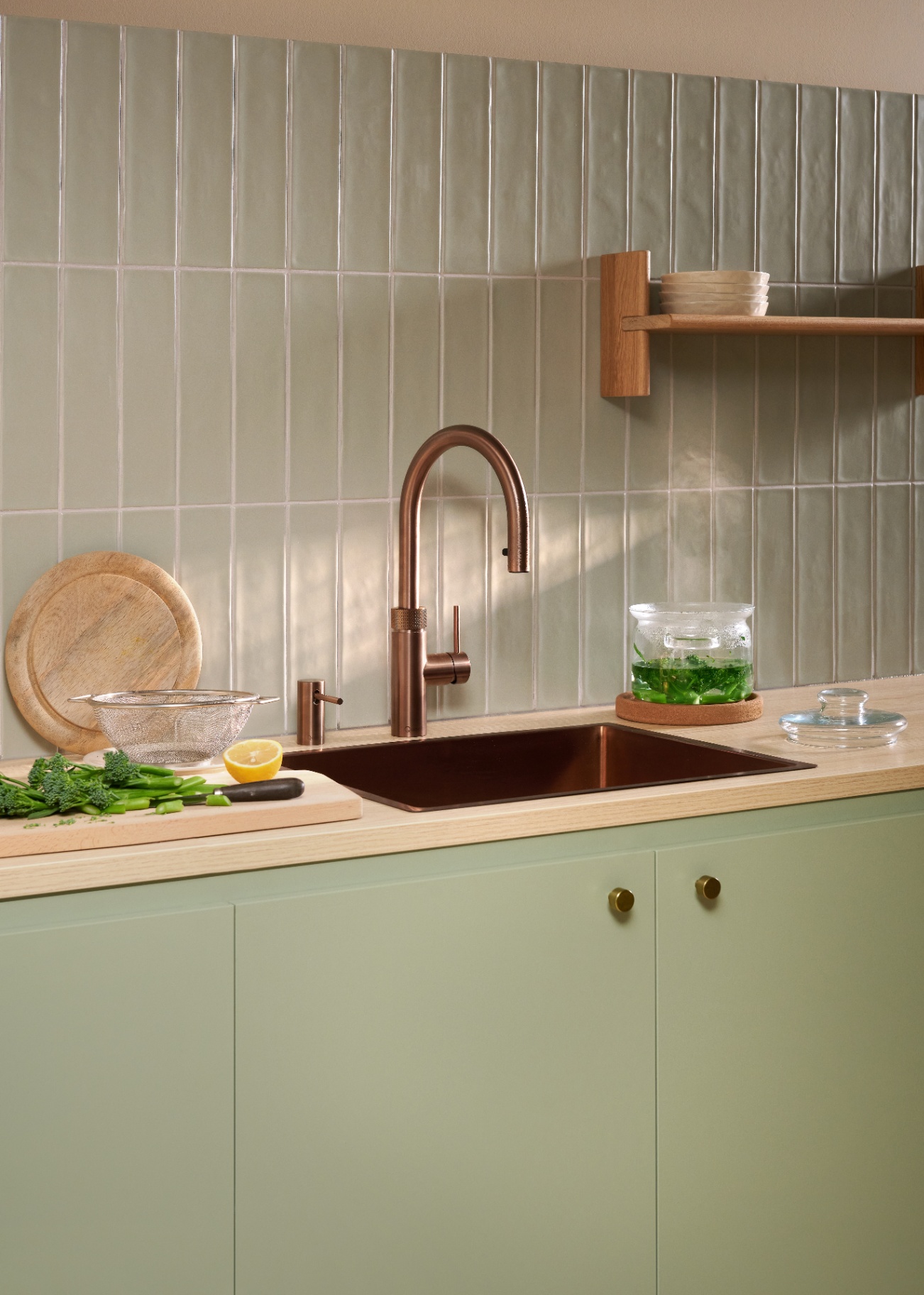 Still life of Flex Round rose copper Quooker with glass pot of blanched broccoli on sage tile kitchen