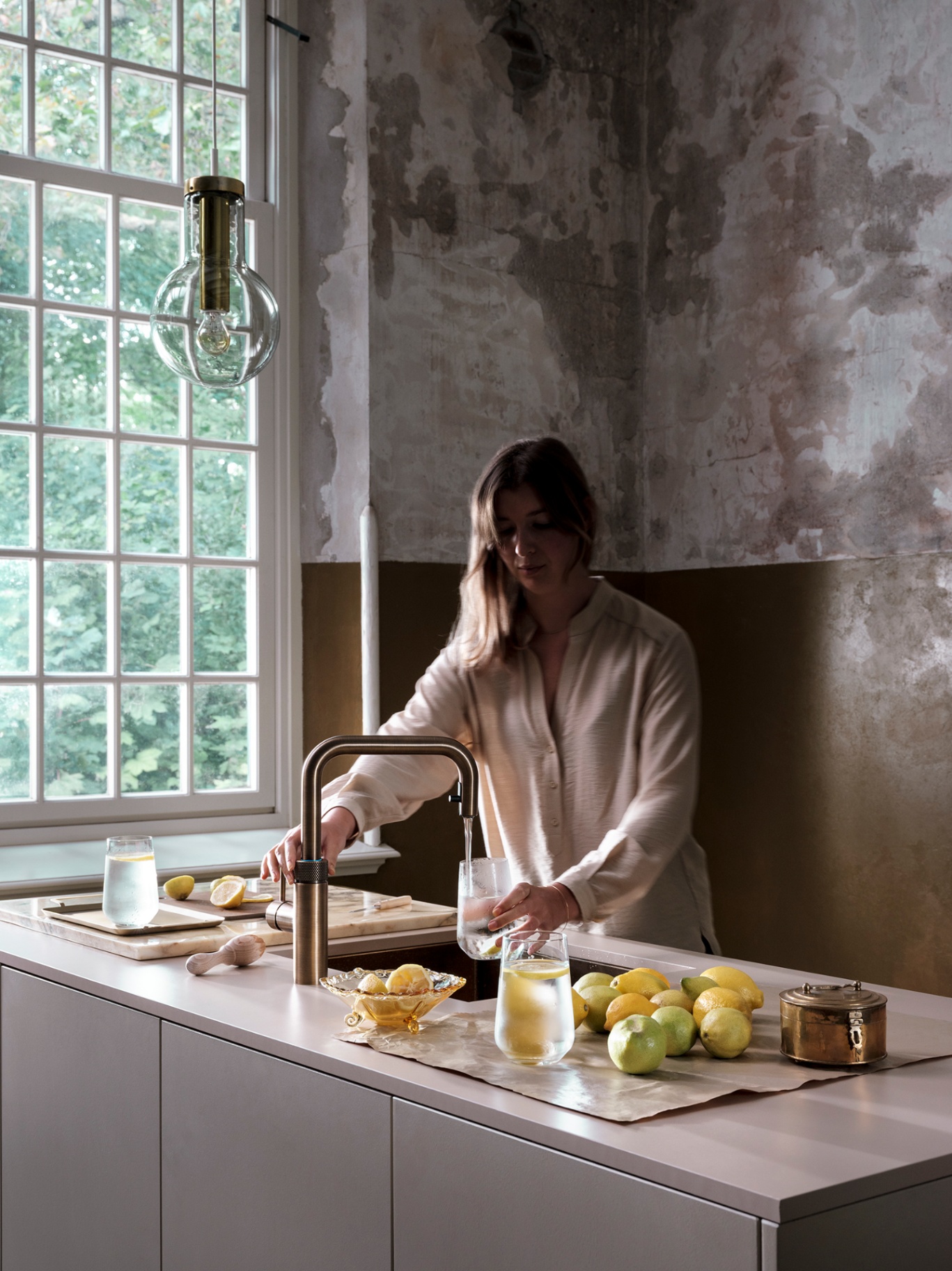 Woman pouring chilled lemon water at a Flex Square patinated brass Quooker in an atelier interior