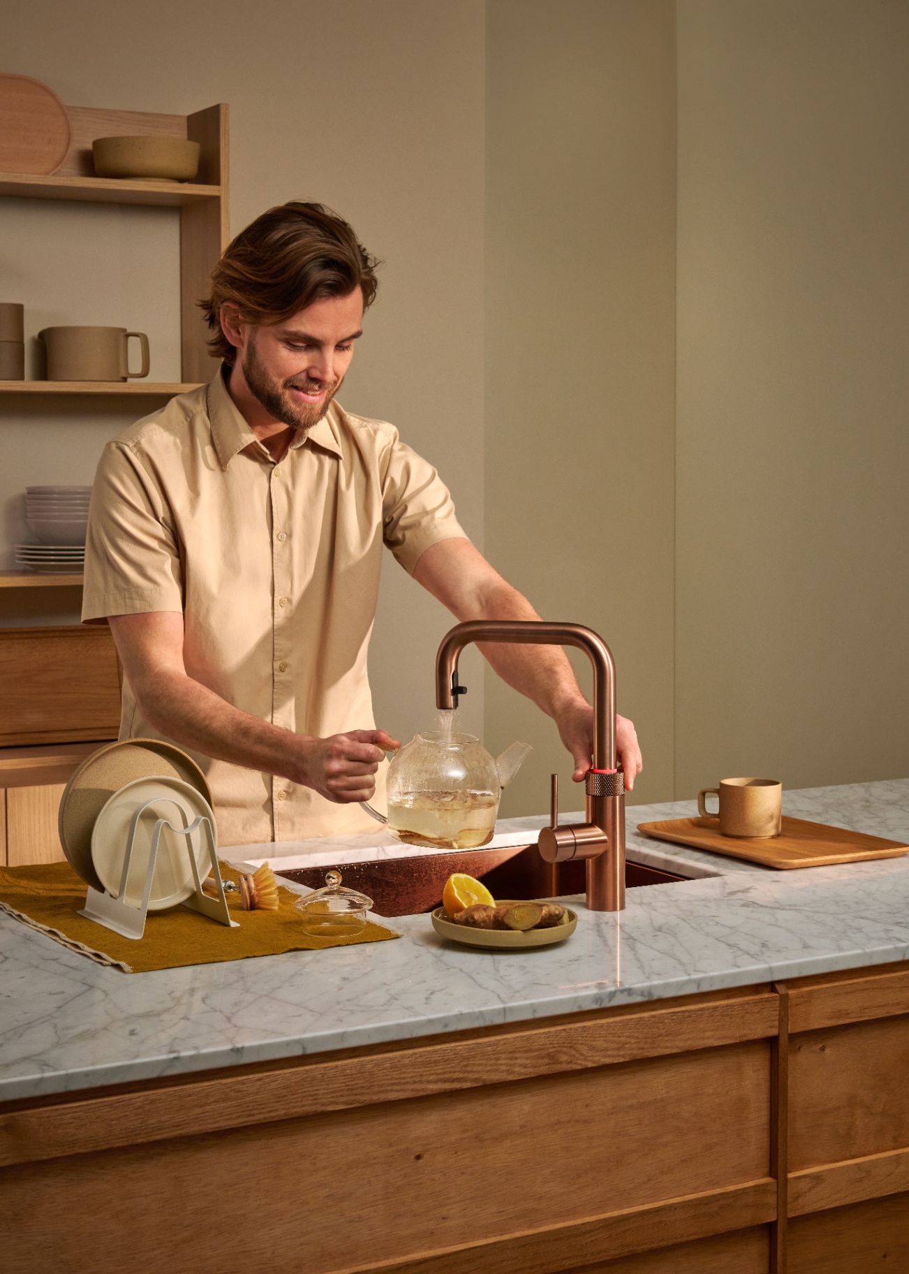 Man brewing ginger tea in a glass teapot at a Flex Square rose copper Quooker on Carrara marble
