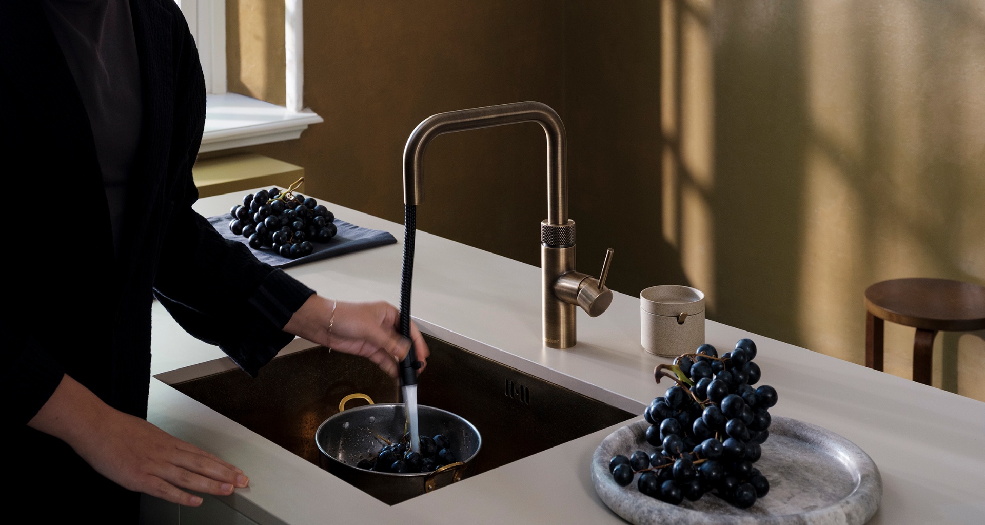 Wide close-up of a Flex Square patinated brass Quooker with pull-out hose rinsing black grapes in an atelier kitchen