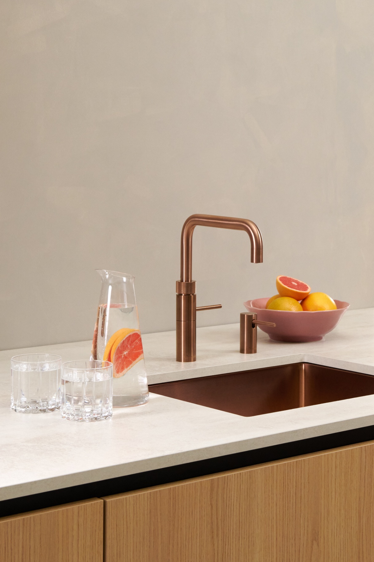 Still life of Quooker Fusion Square rose copper tap with grapefruit carafe on stone worktop