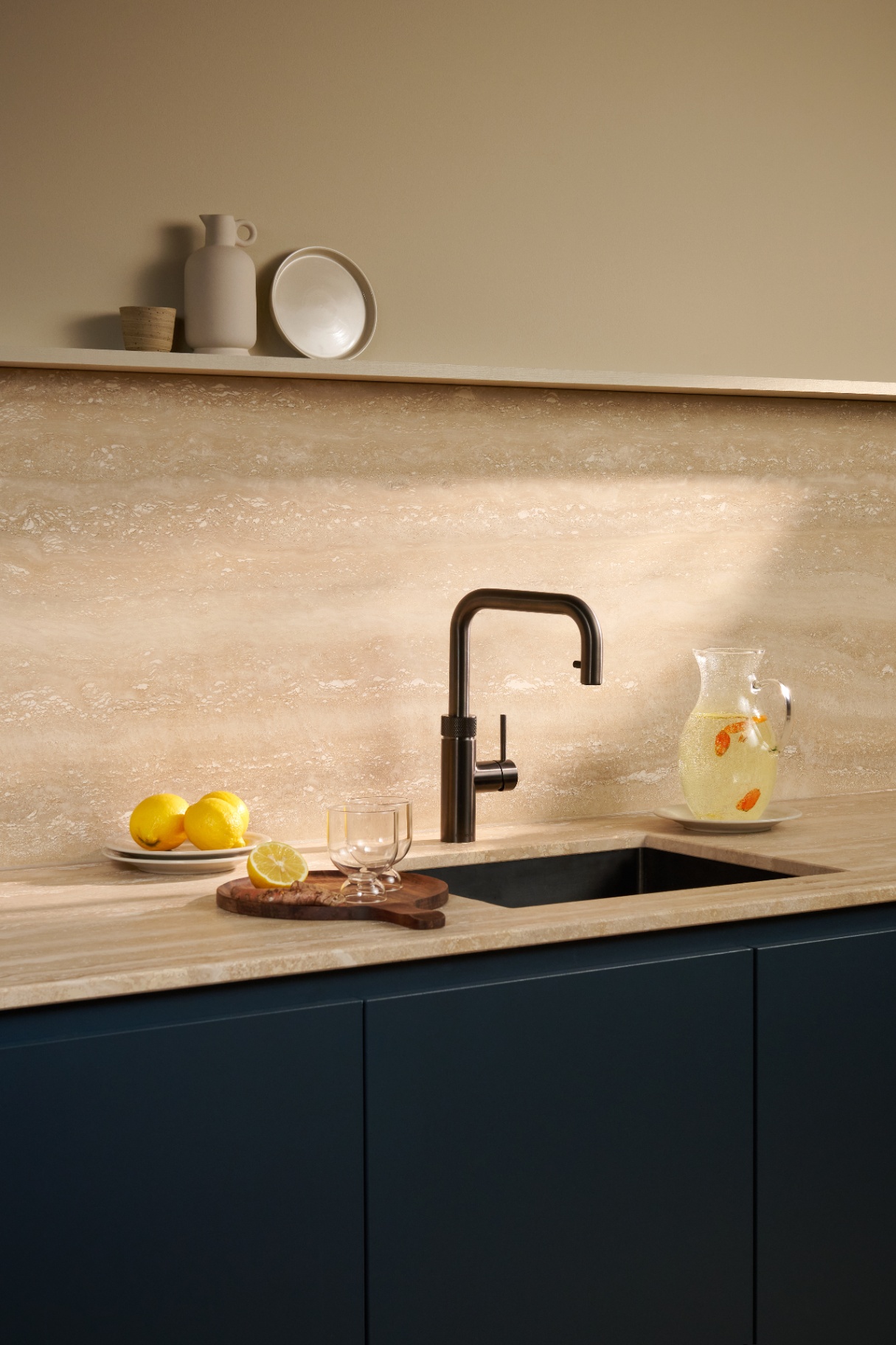 Editorial still life of a Flex Square gun metal Quooker with lemon-turmeric carafe on travertine