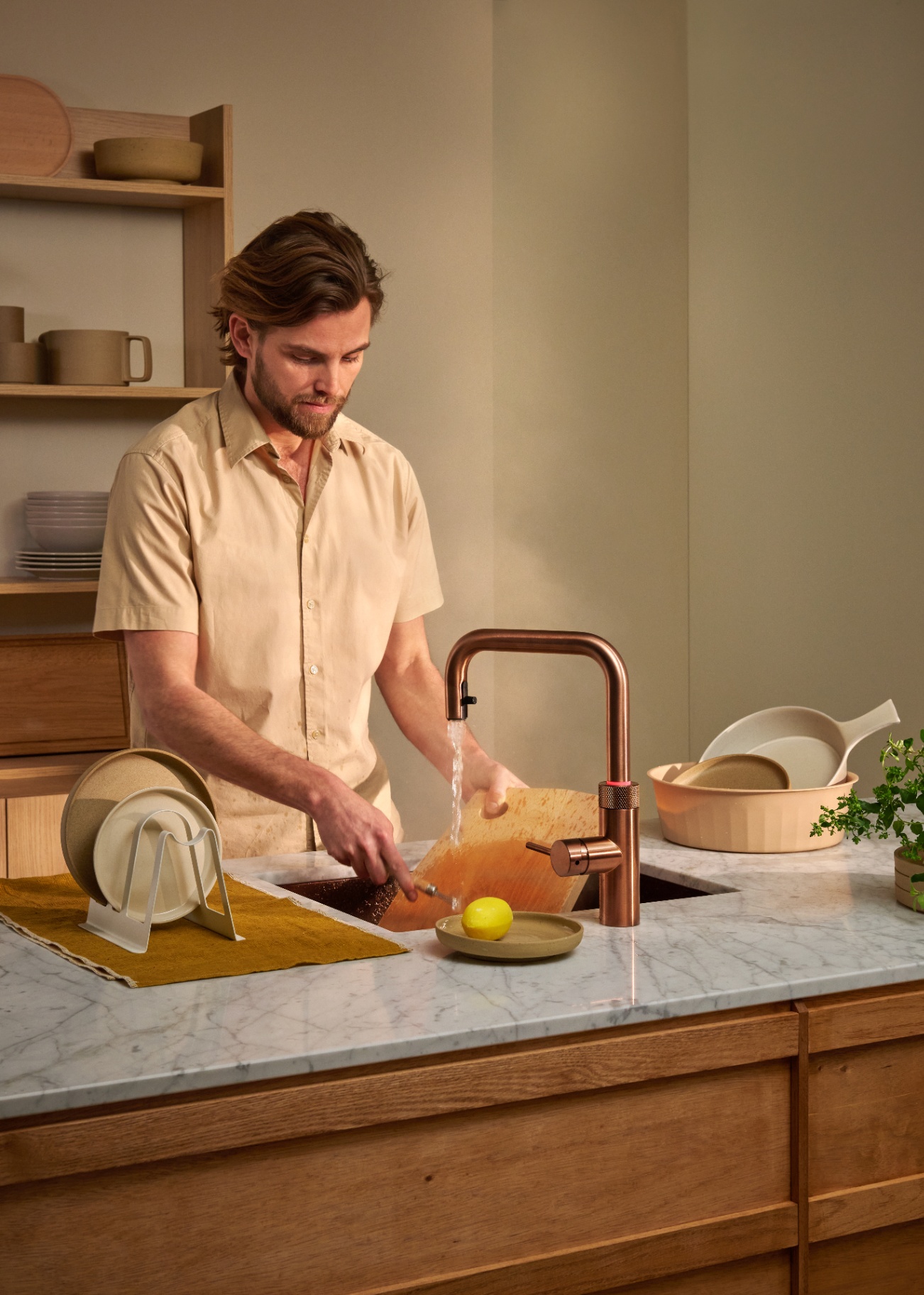 Man rinsing a wooden cutting board under a Flex Square rose copper Quooker in a marble kitchen